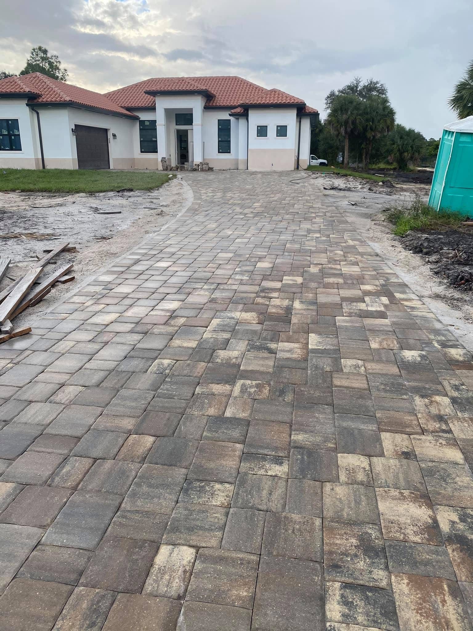 Brick driveway leading to a white house with a red roof on a cloudy day