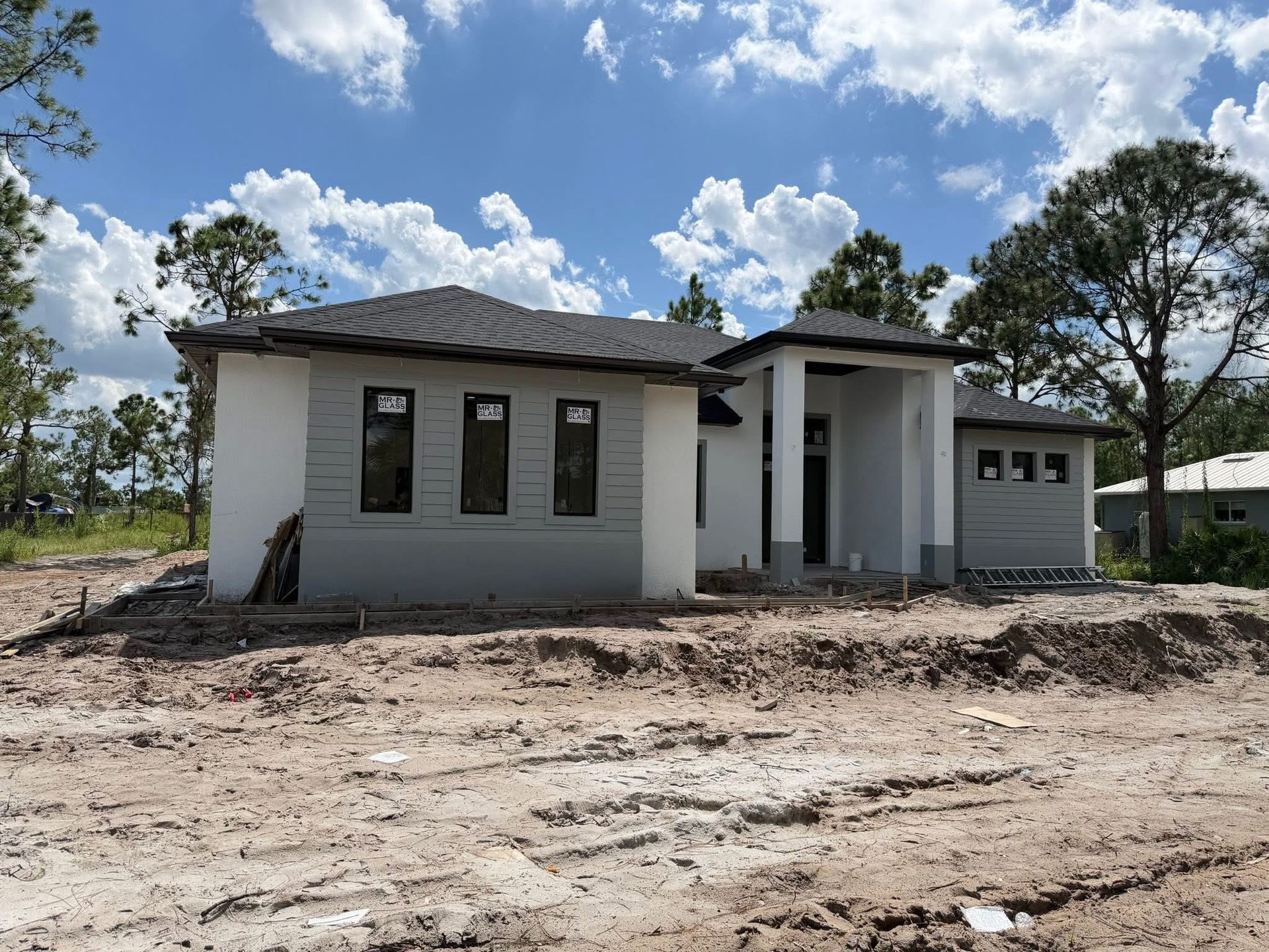 New white house under construction with garage, front porch, and dirt lot under a blue sky