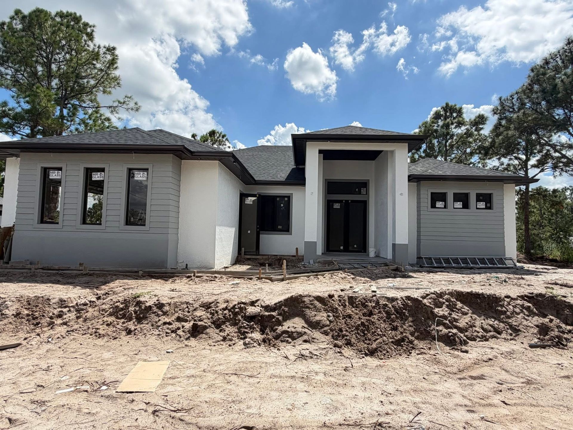 New single-story house under construction with gray siding, white trim, and a front porch under a blue sky