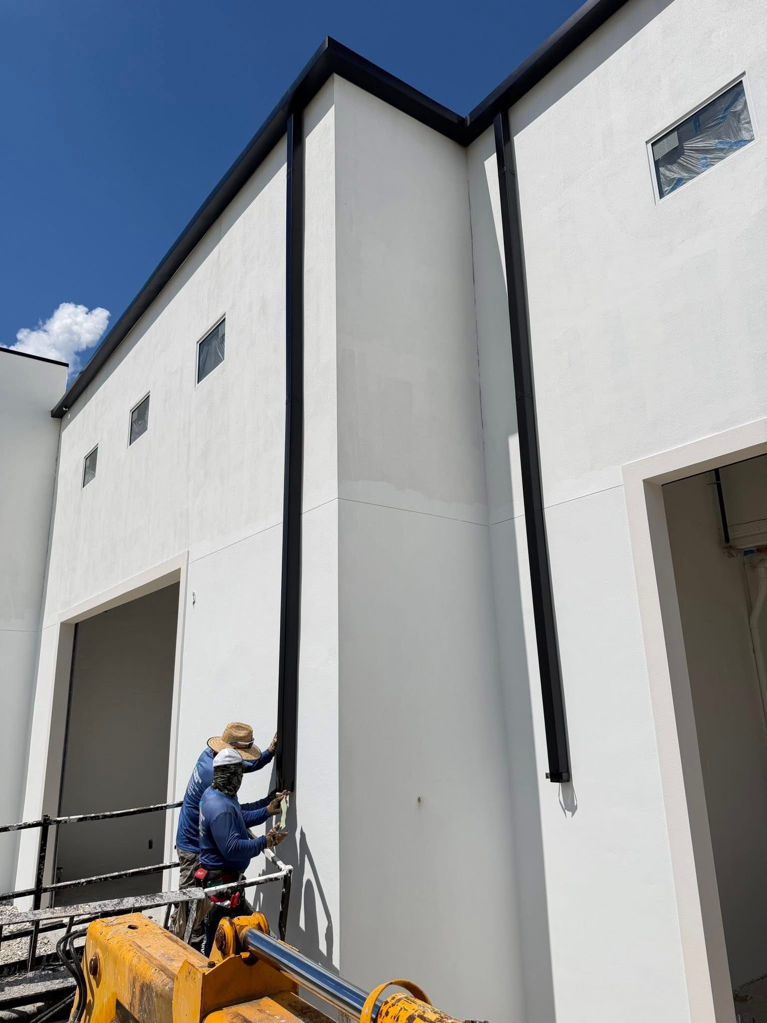 Worker on a lift painting a tall white building exterior under a blue sky