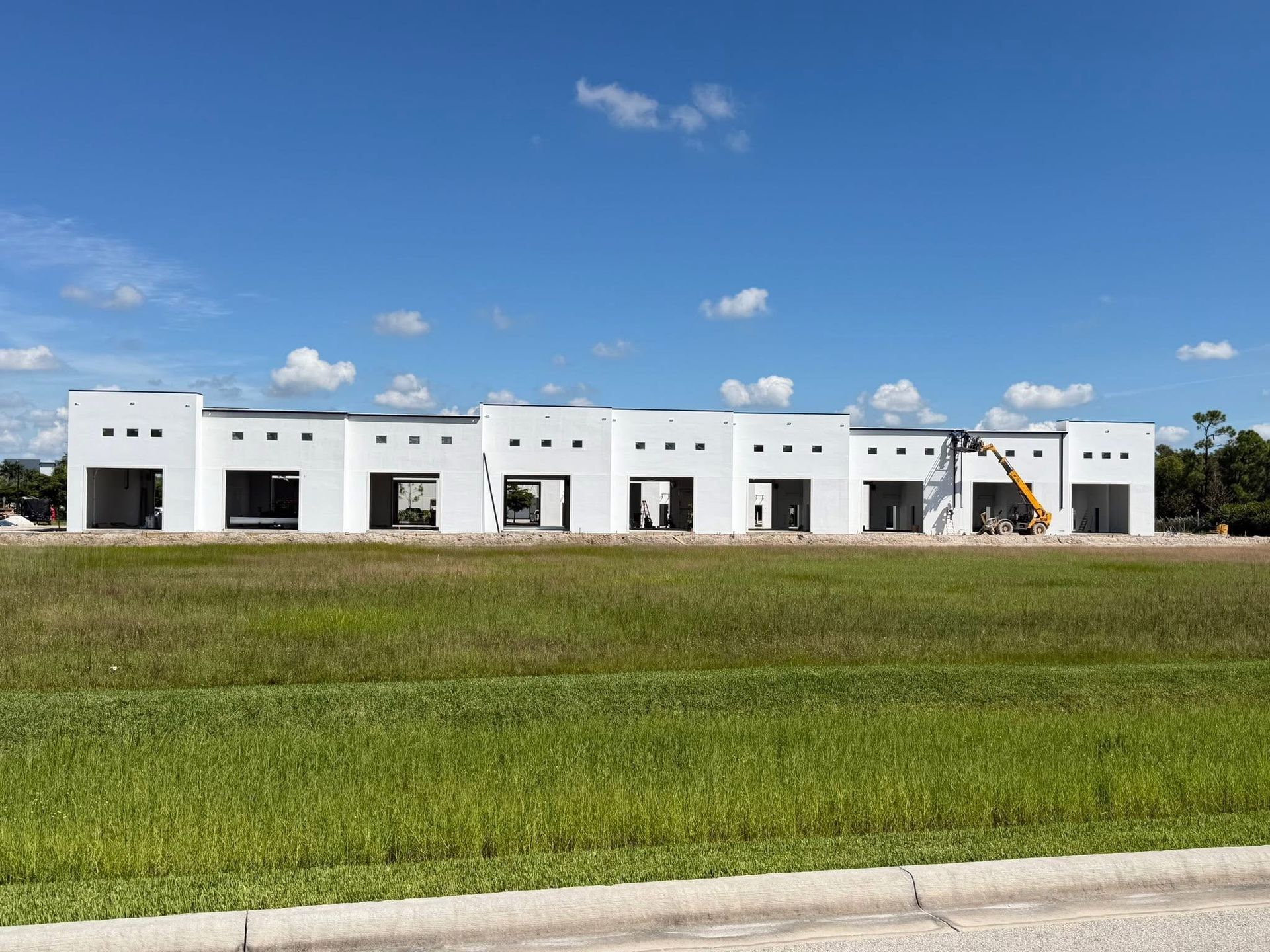 White modular building under construction on a grassy field under a blue sky