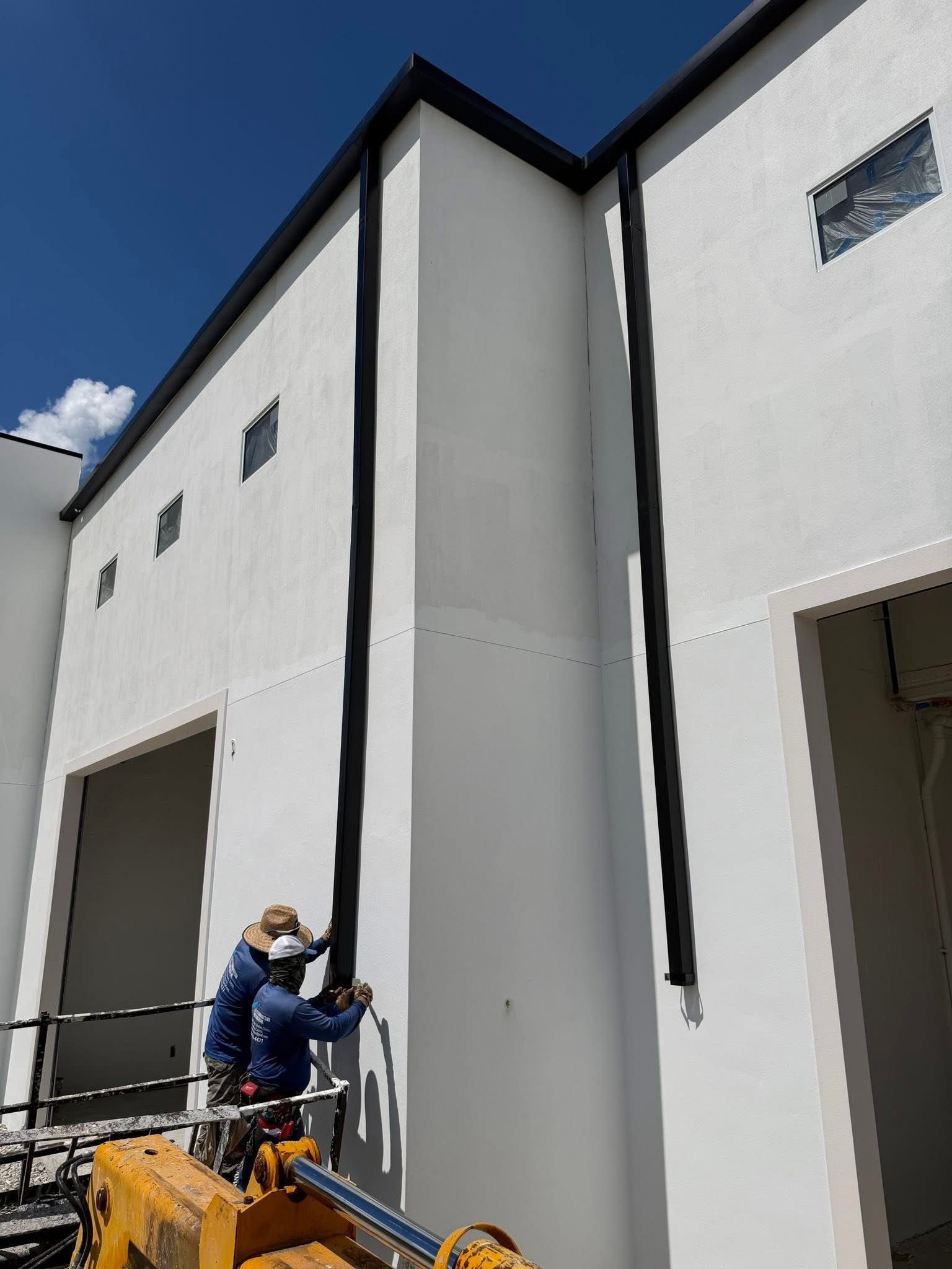 Worker on a lift painting a tall white building exterior under a blue sky