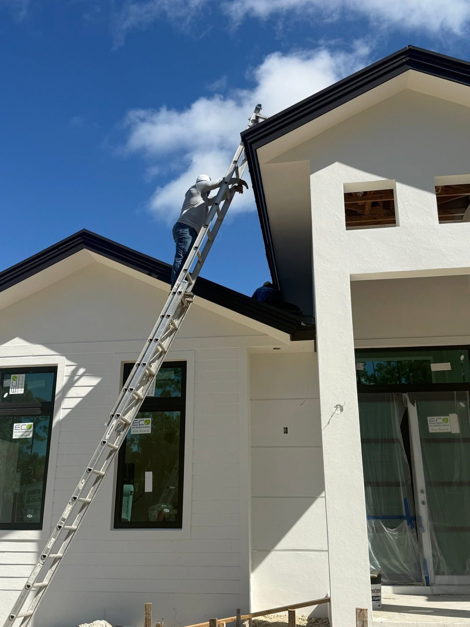 Extension ladder leaning from one house roof to another on a residential building exterior.