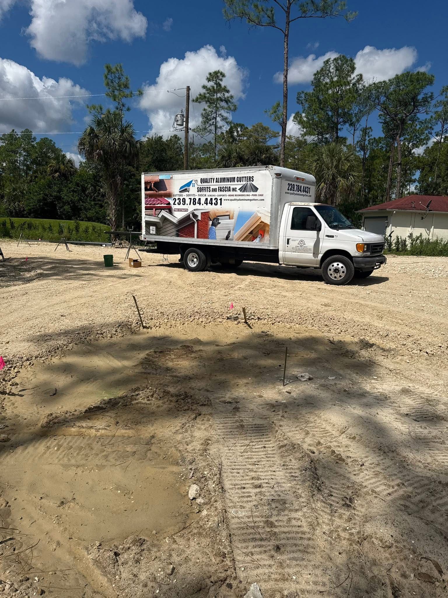 White box truck with company graphics parked on a sandy lot under a blue sky with trees nearby