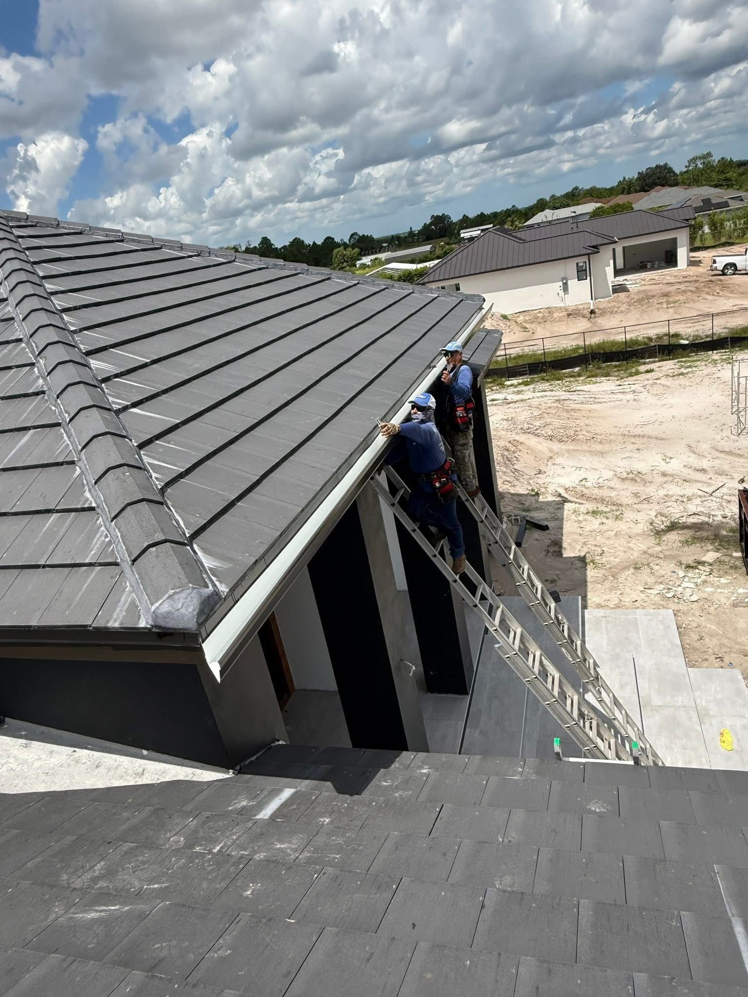 Workers on a rooftop beside ladders at a house construction site under a cloudy sky
