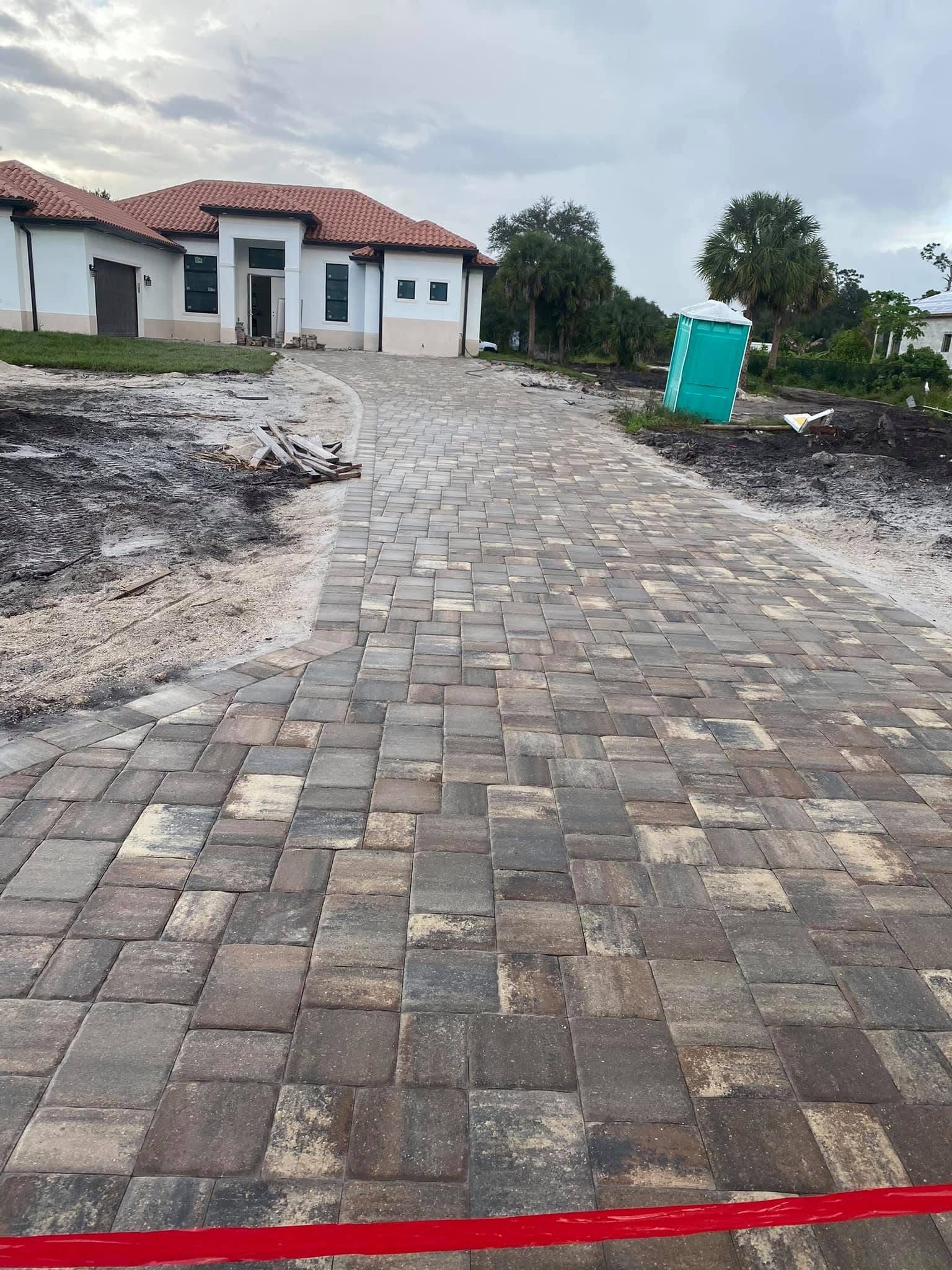 Brick-paved driveway leading to a white house with a red roof, under cloudy skies