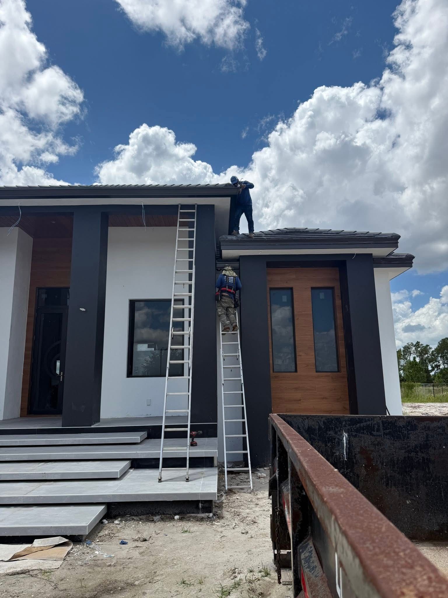 Modern house exterior with white and wood panels, cloudy sky, and a ladder leaning by the front entrance
