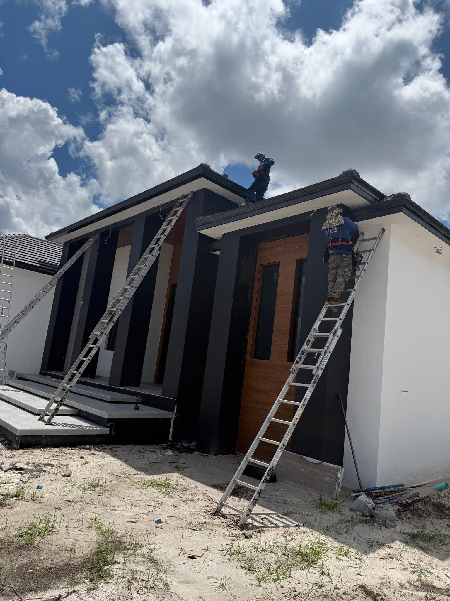 Damaged house exterior with bent roof supports and ladders leaning against the front under cloudy sky