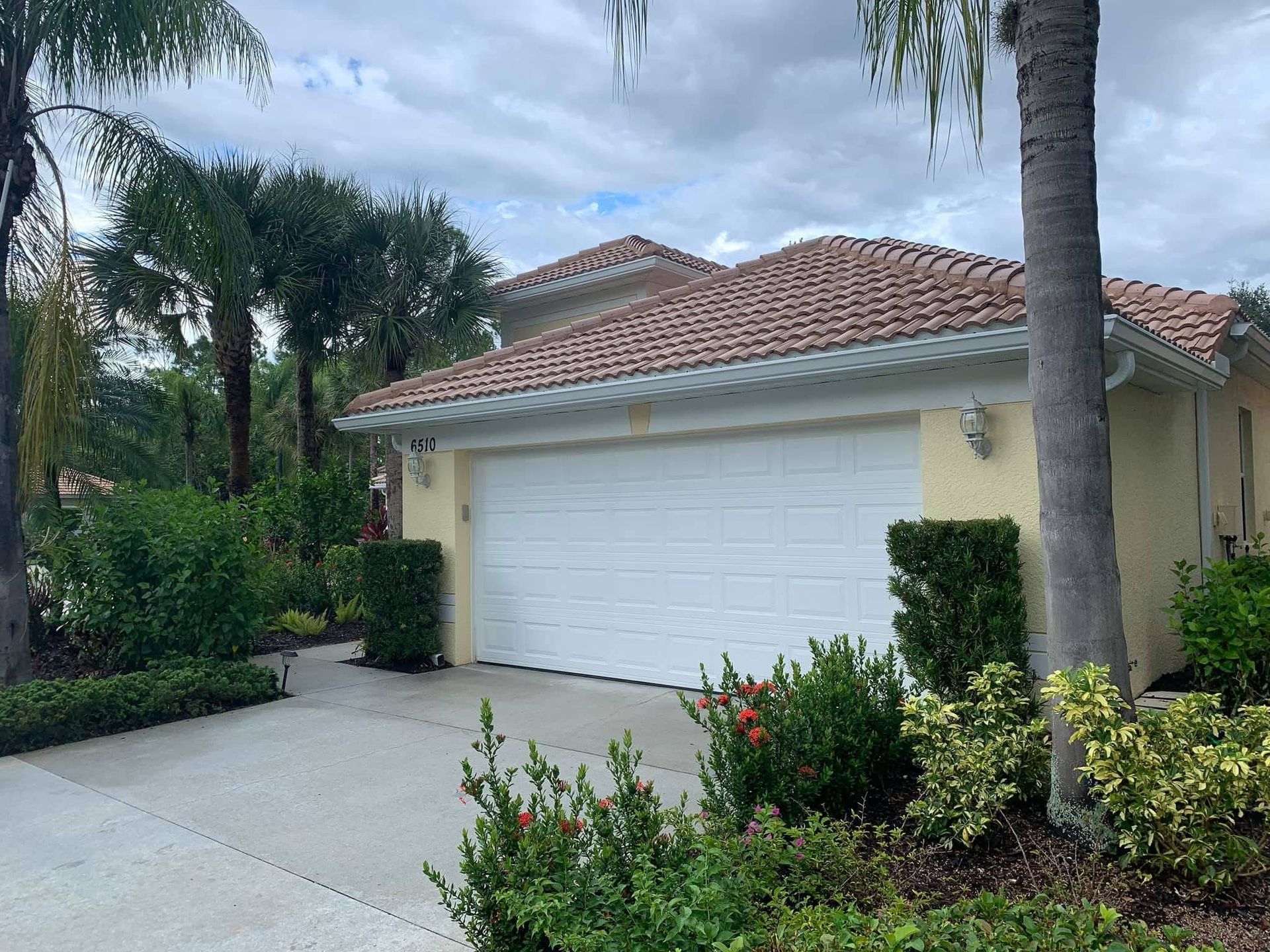 Suburban house with white garage, red tile roof, and landscaped front yard surrounded by palm trees