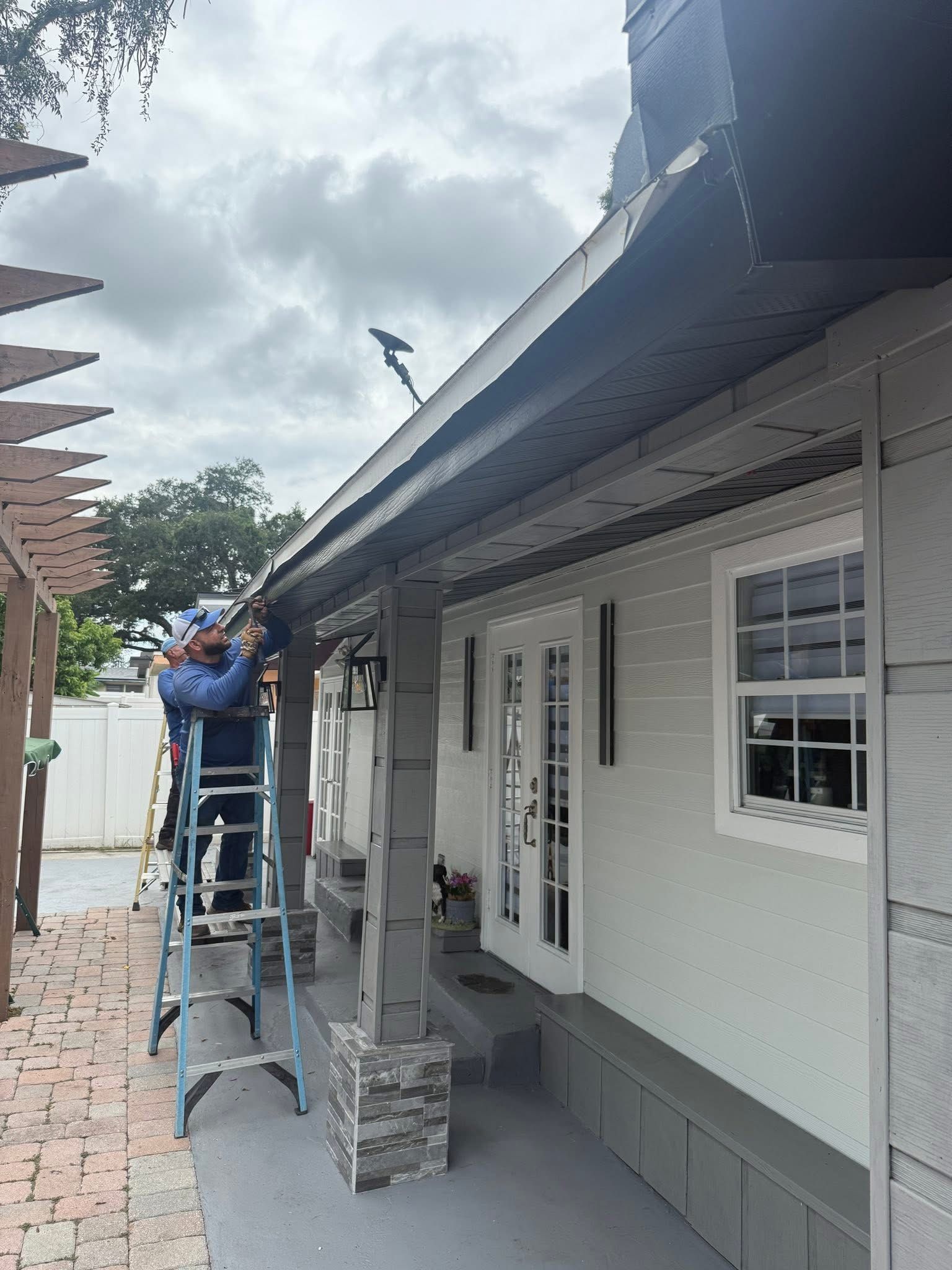 Worker on a ladder repairing the roof gutter beside a white house