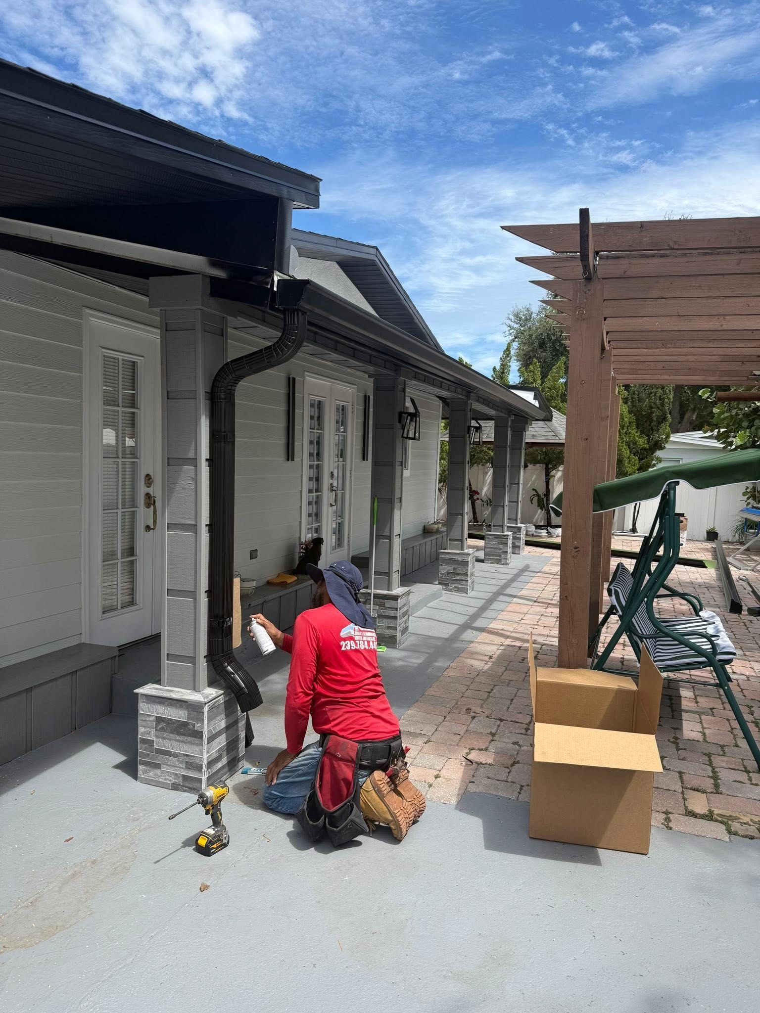 Person in red jacket kneels beside a dog on a sidewalk between gray houses and stacked boxes