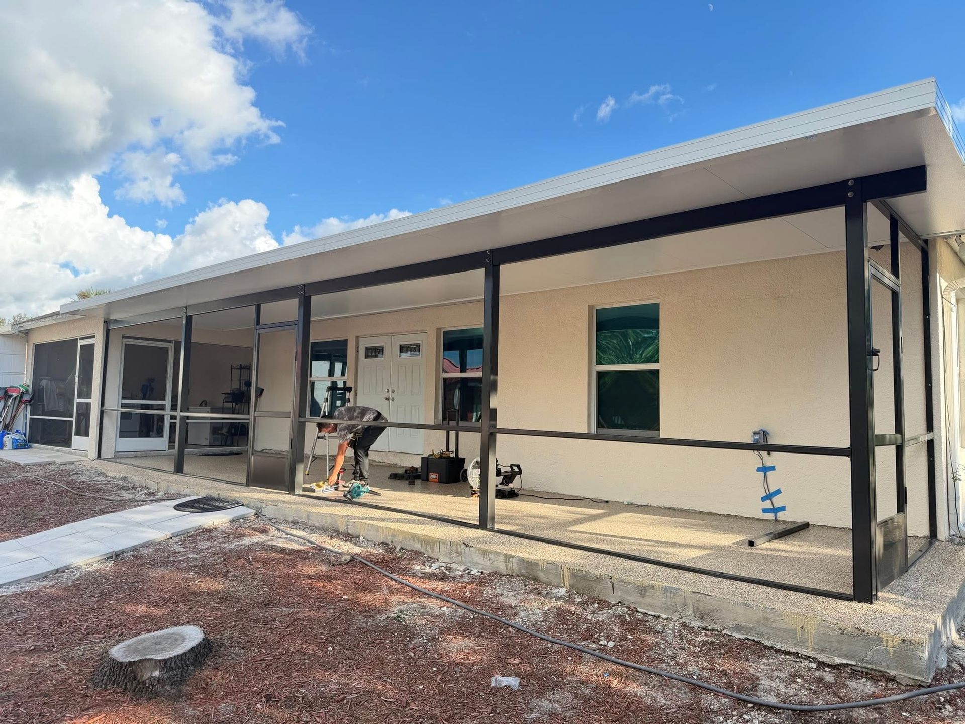 Single-story building under construction with a covered porch, beige walls, and exposed supports.
