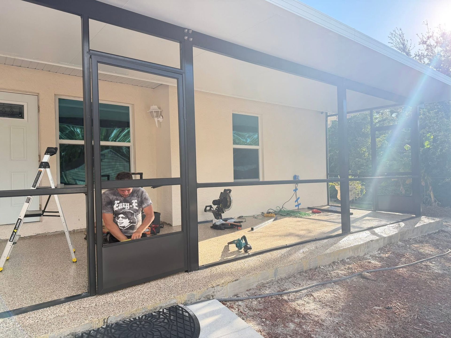 Worker assembling black metal screen enclosure outside a beige house