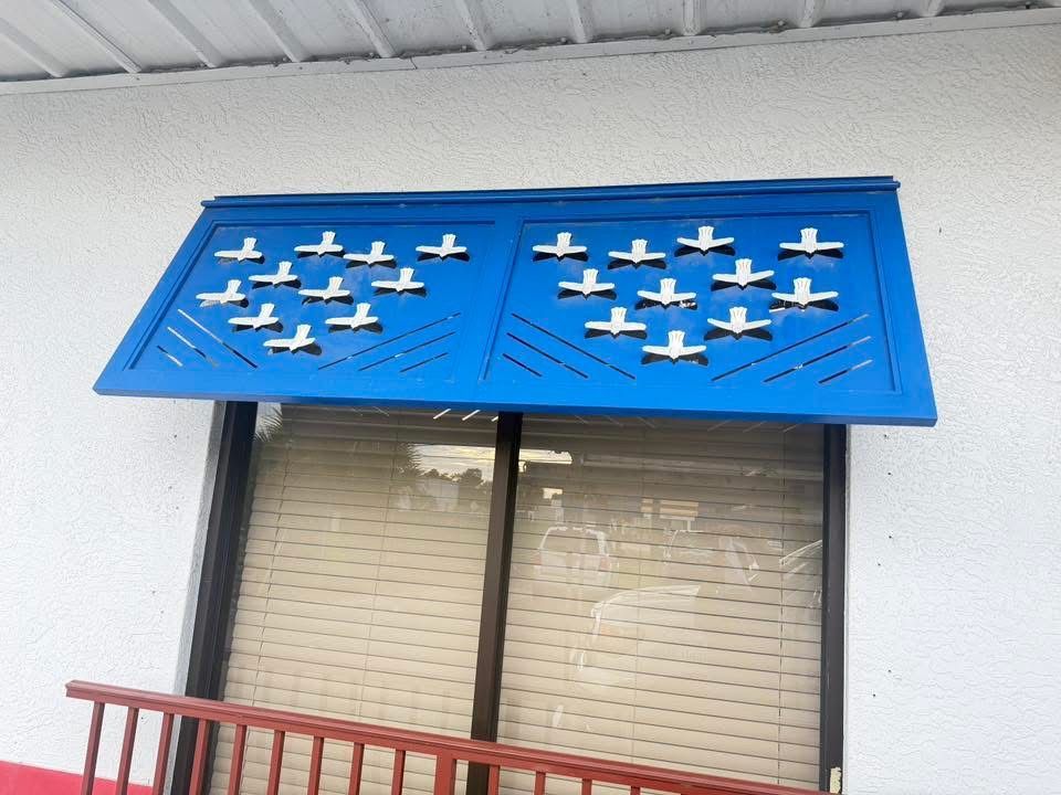 Blue metal awning with white bird cutouts above a window and red railing below