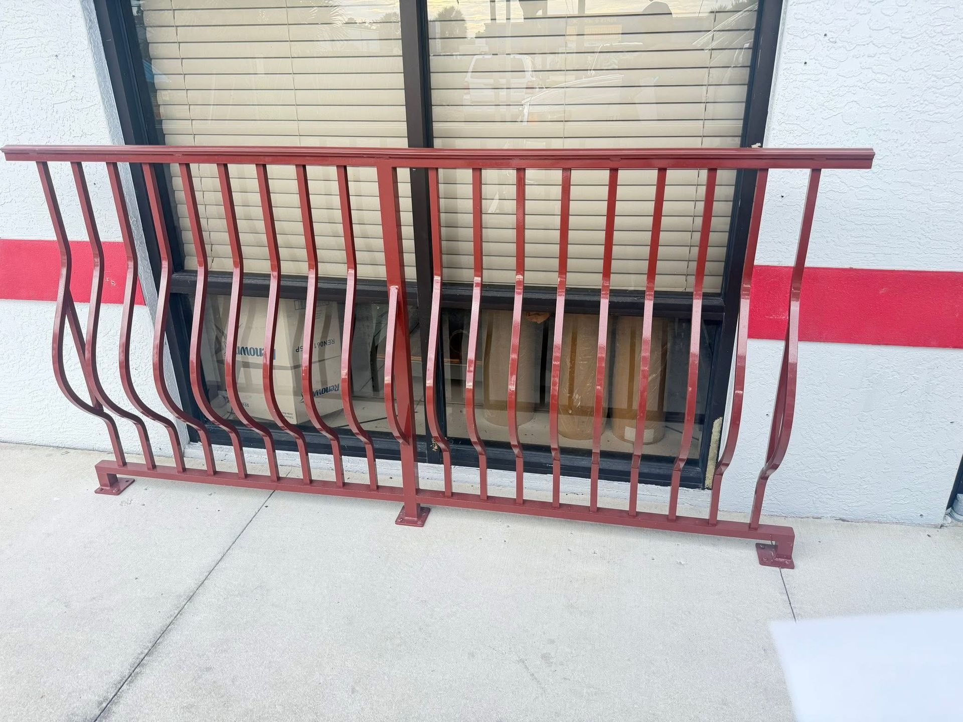 Red metal railing in front of a closed storefront window with a red stripe on the wall