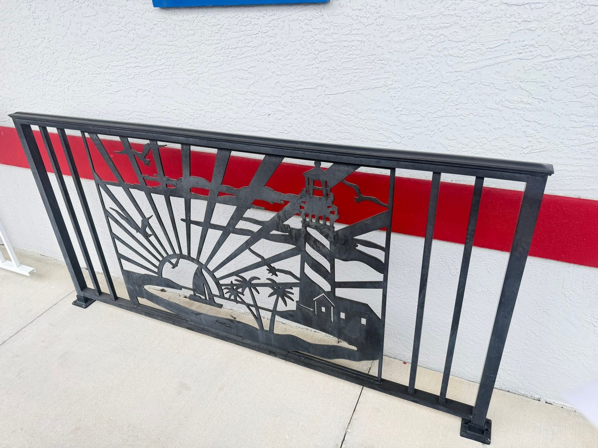 Black metal railing with sunburst and cactus cutout against a white wall with a red stripe