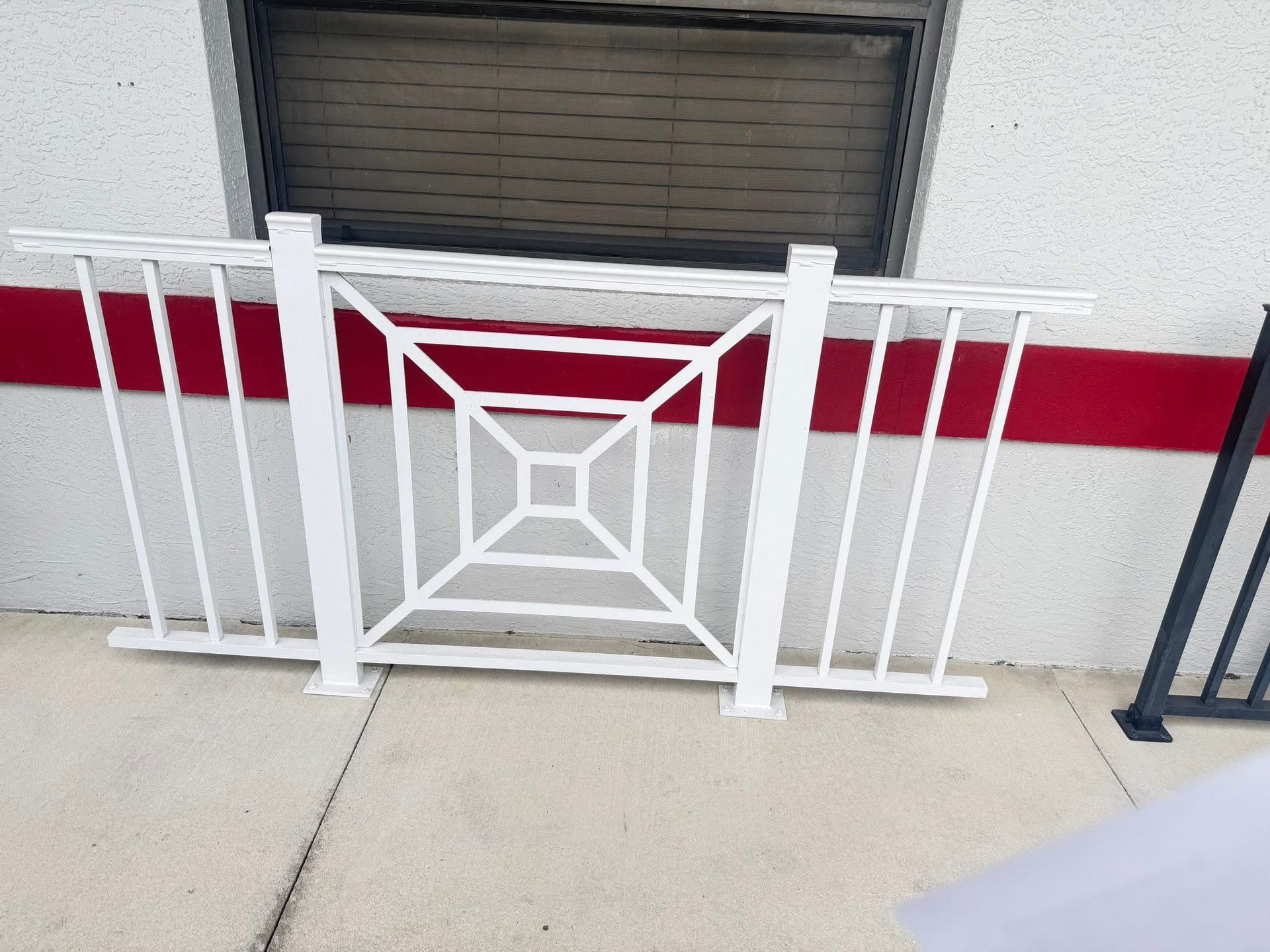 White metal railing with geometric center pattern in front of a building wall and window vent.