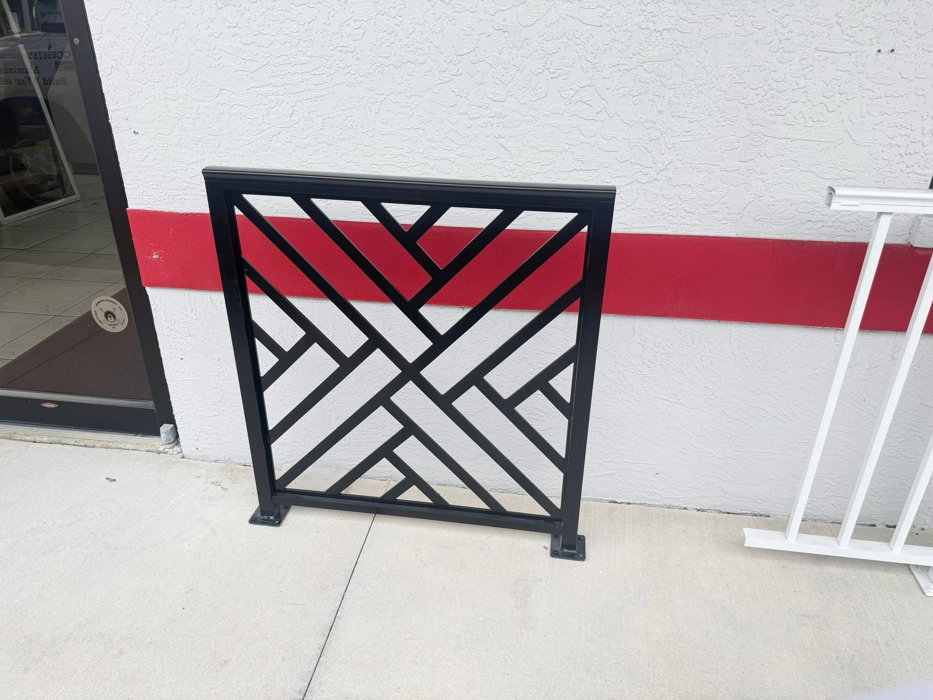 Black metal geometric gate with red and white diagonal panels against a white wall