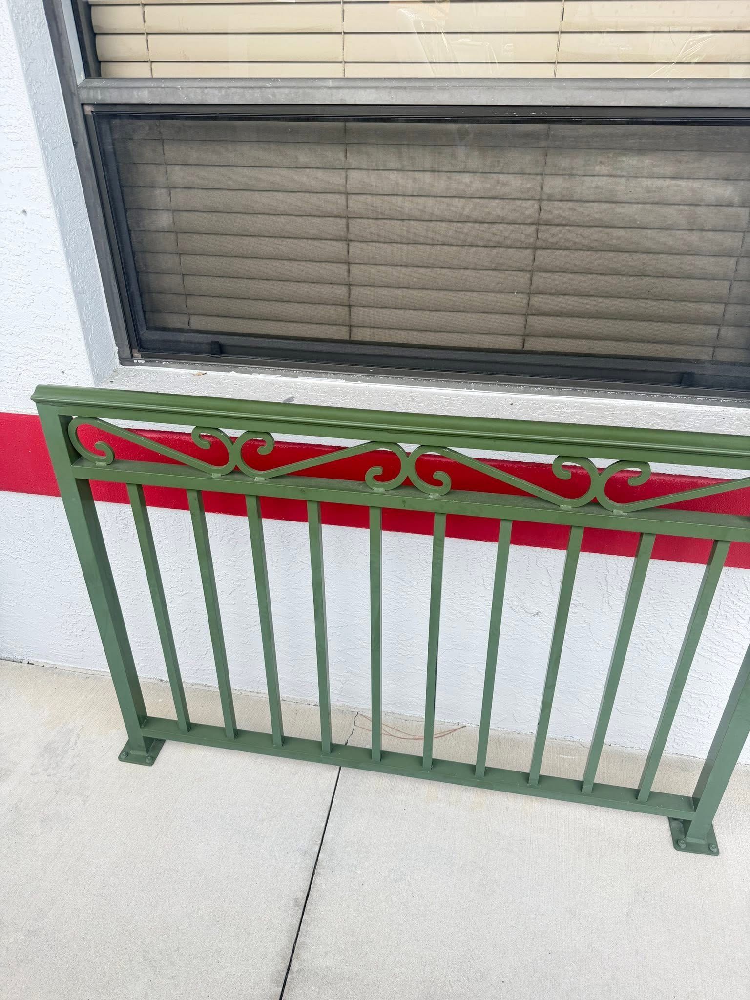 Green metal railing with a red decorative top in front of a window on a porch