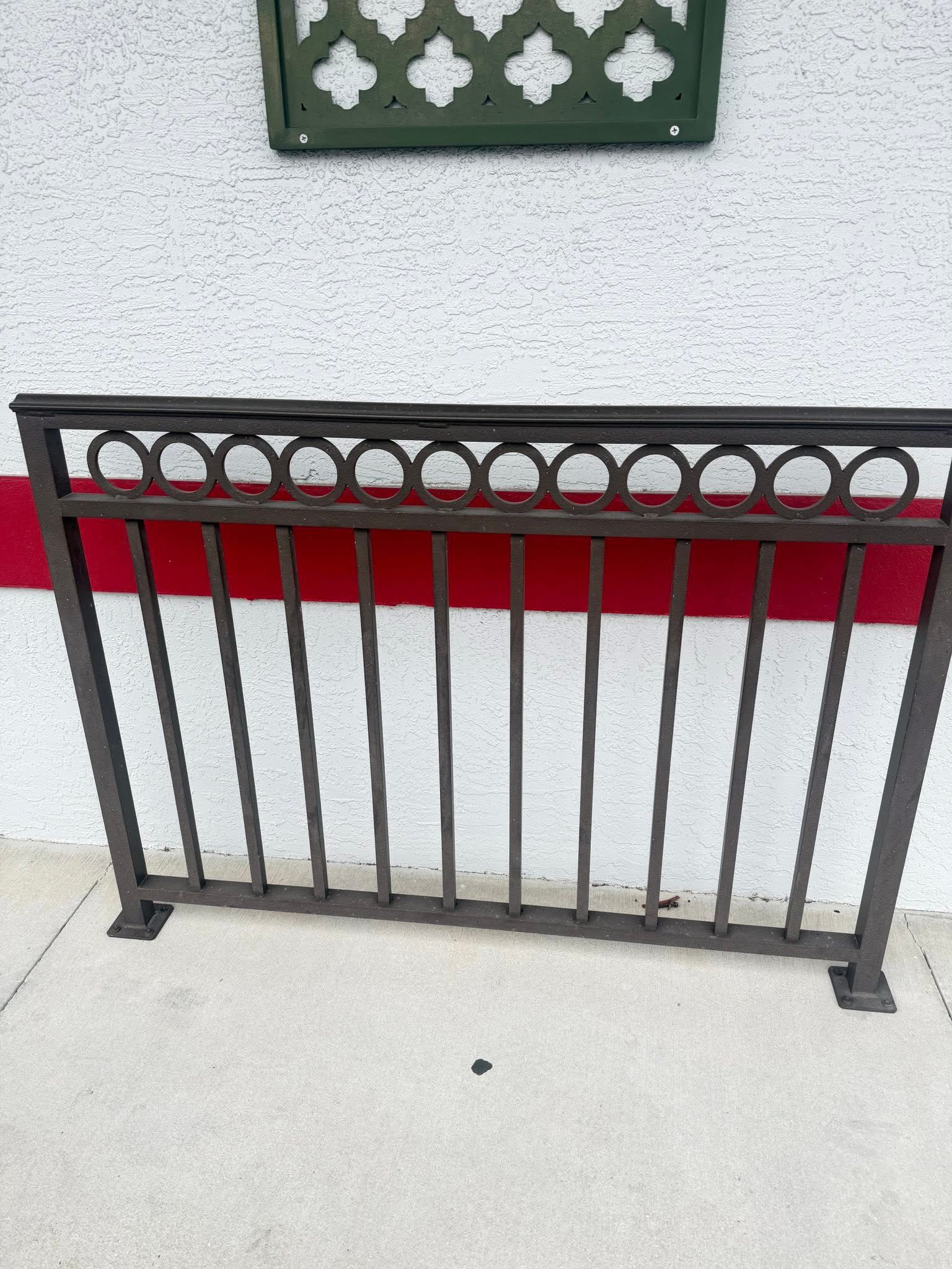 Black metal railing in front of a light gray wall with a red stripe.