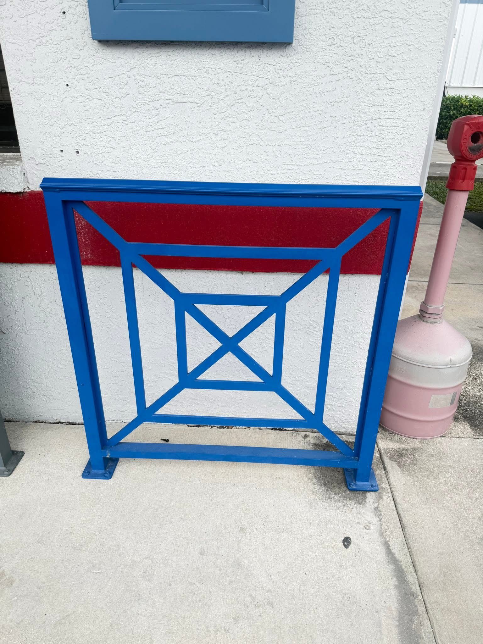 Blue and red decorative metal barrier on a sidewalk beside a red pipe and pink post