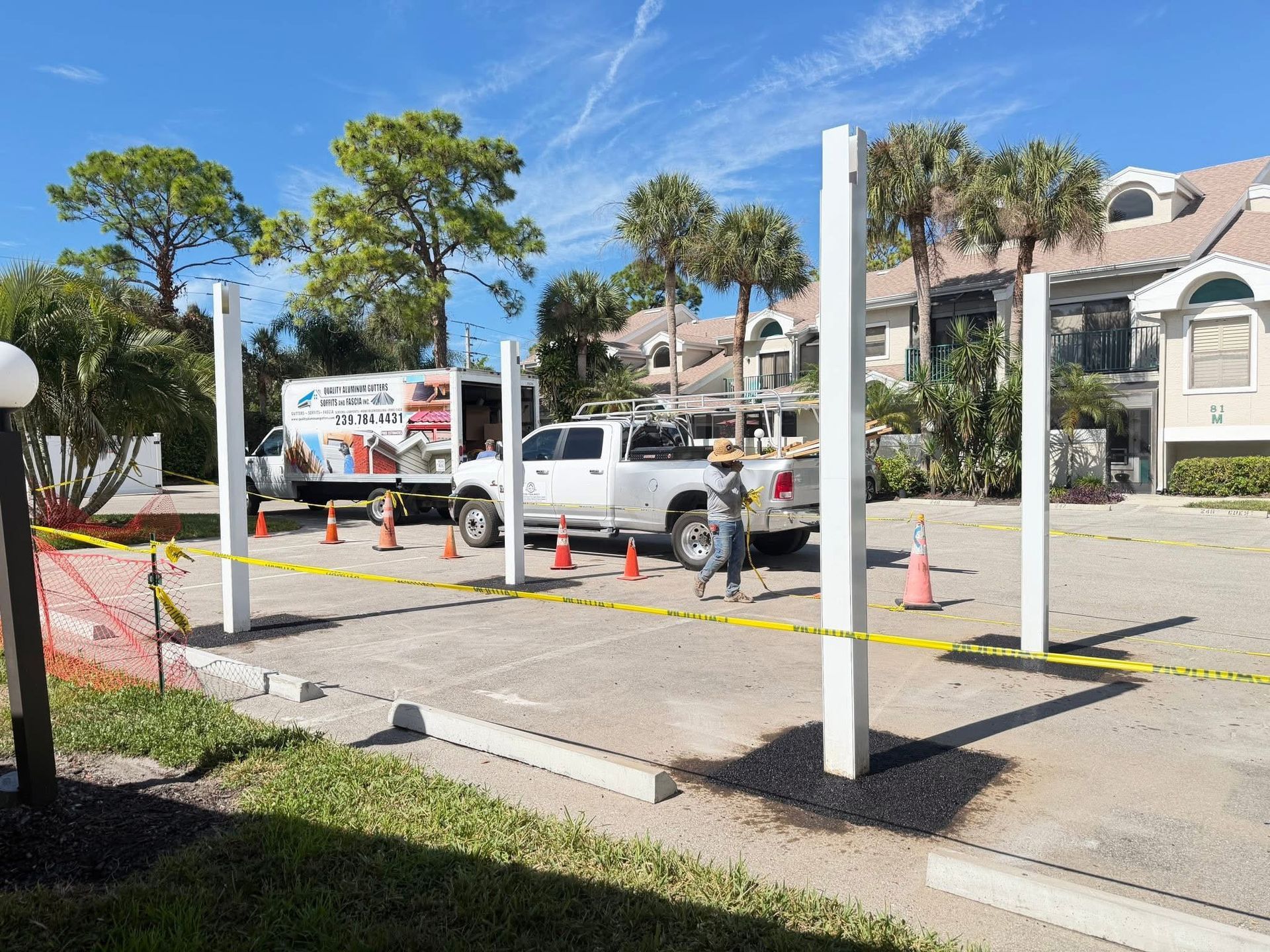 Construction cones and caution tape around a parking lot with a white van and palm trees nearby.