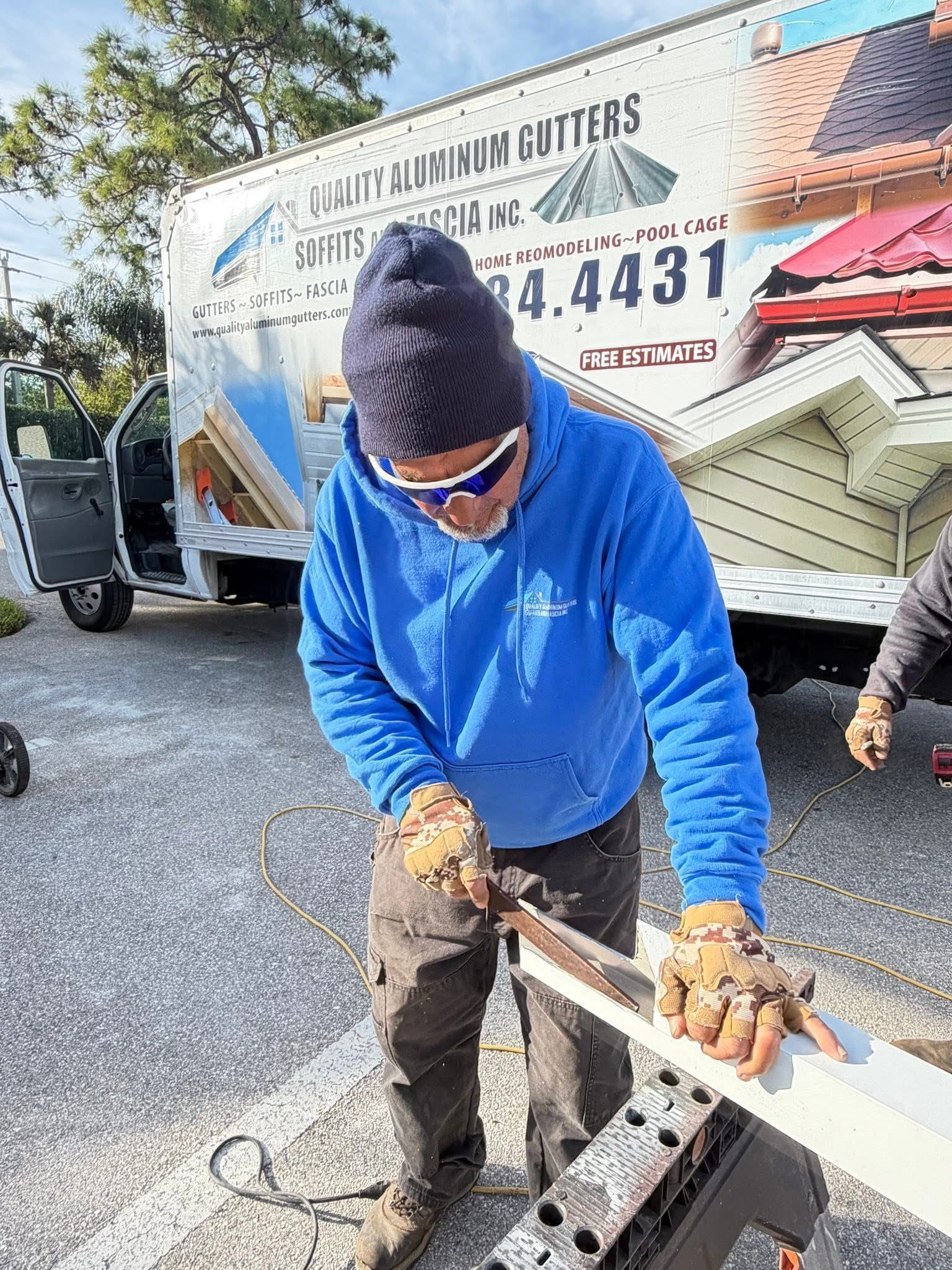 Worker in blue hoodie cutting a white gutter outside a van on a driveway