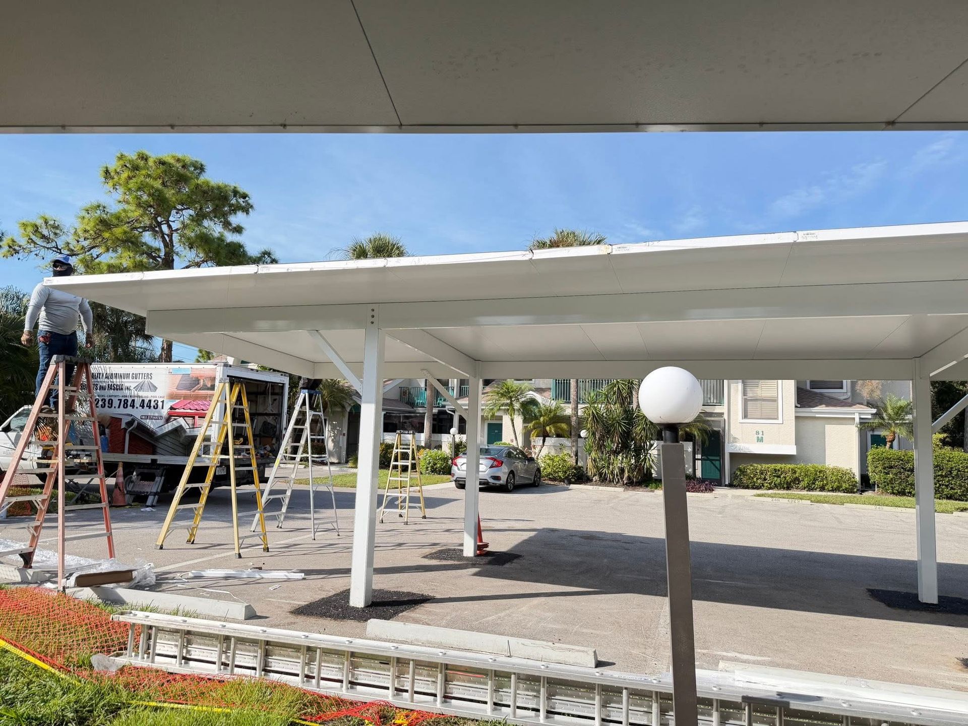 Outdoor pavilion construction with white roof, ladders, scaffolding, and workers in a parking lot