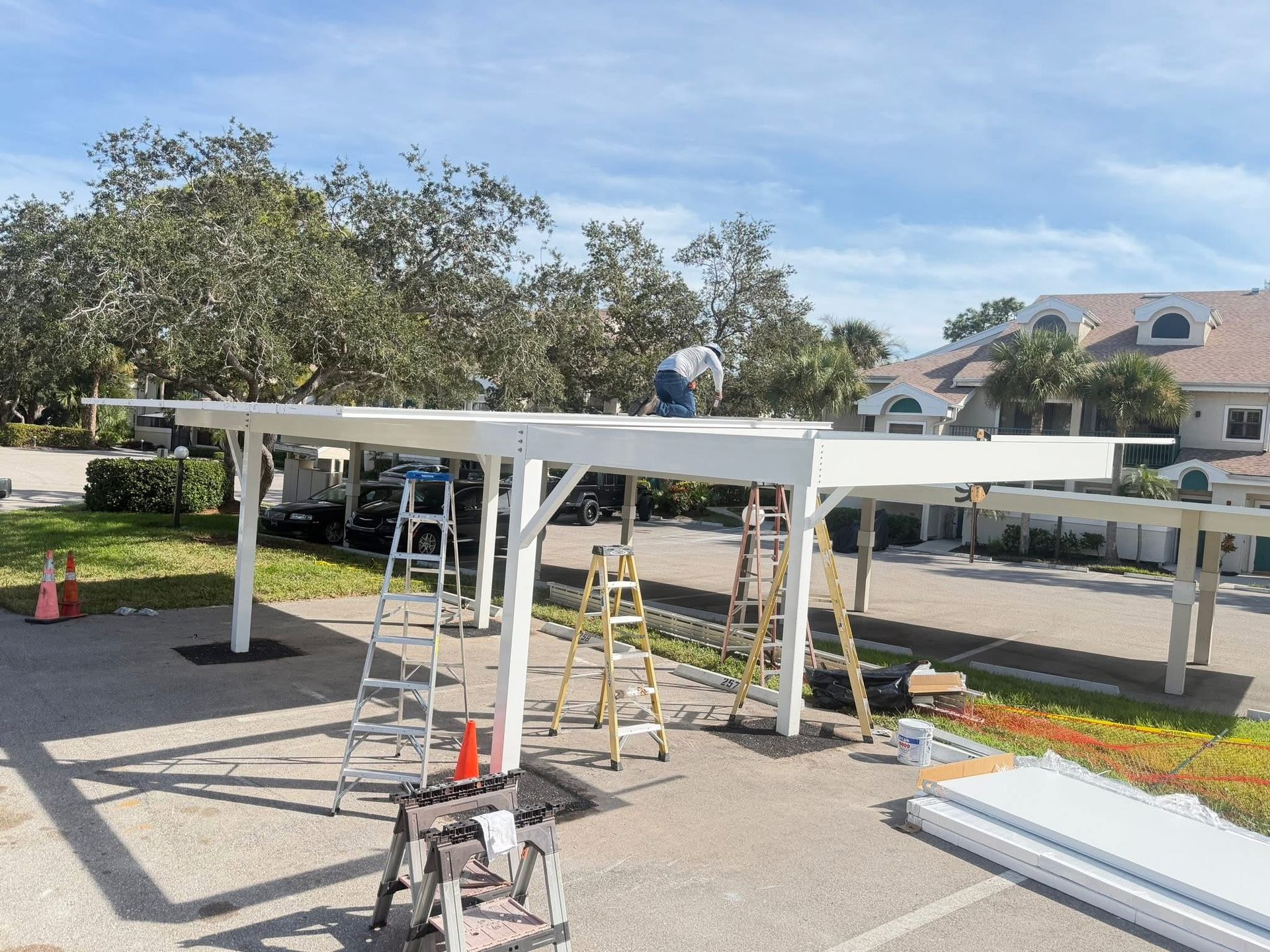 Workers assembling a white pergola frame in a sunny suburban yard with ladders and tools