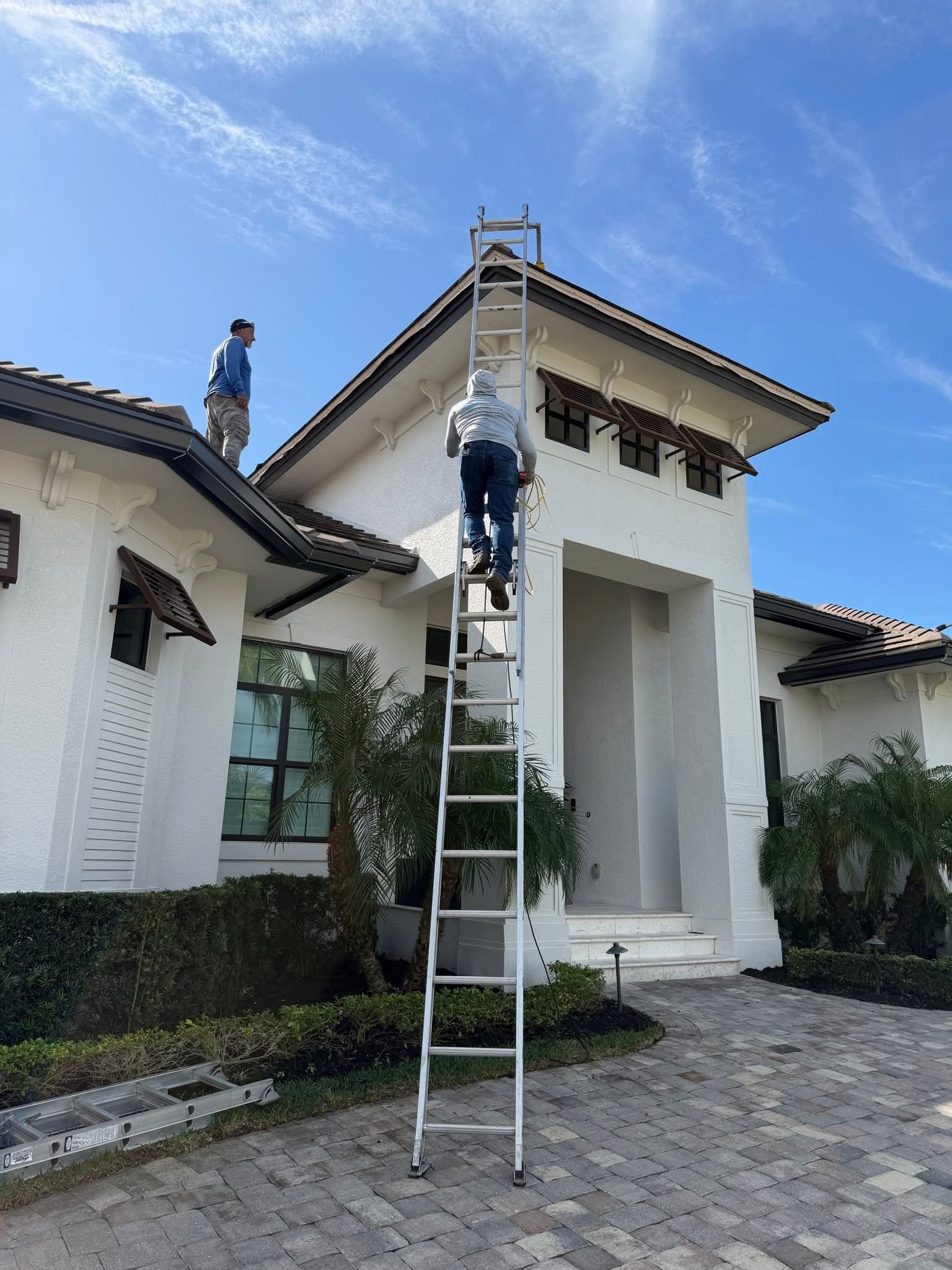 Workers on ladders painting the exterior of a white house with a tiled roof.