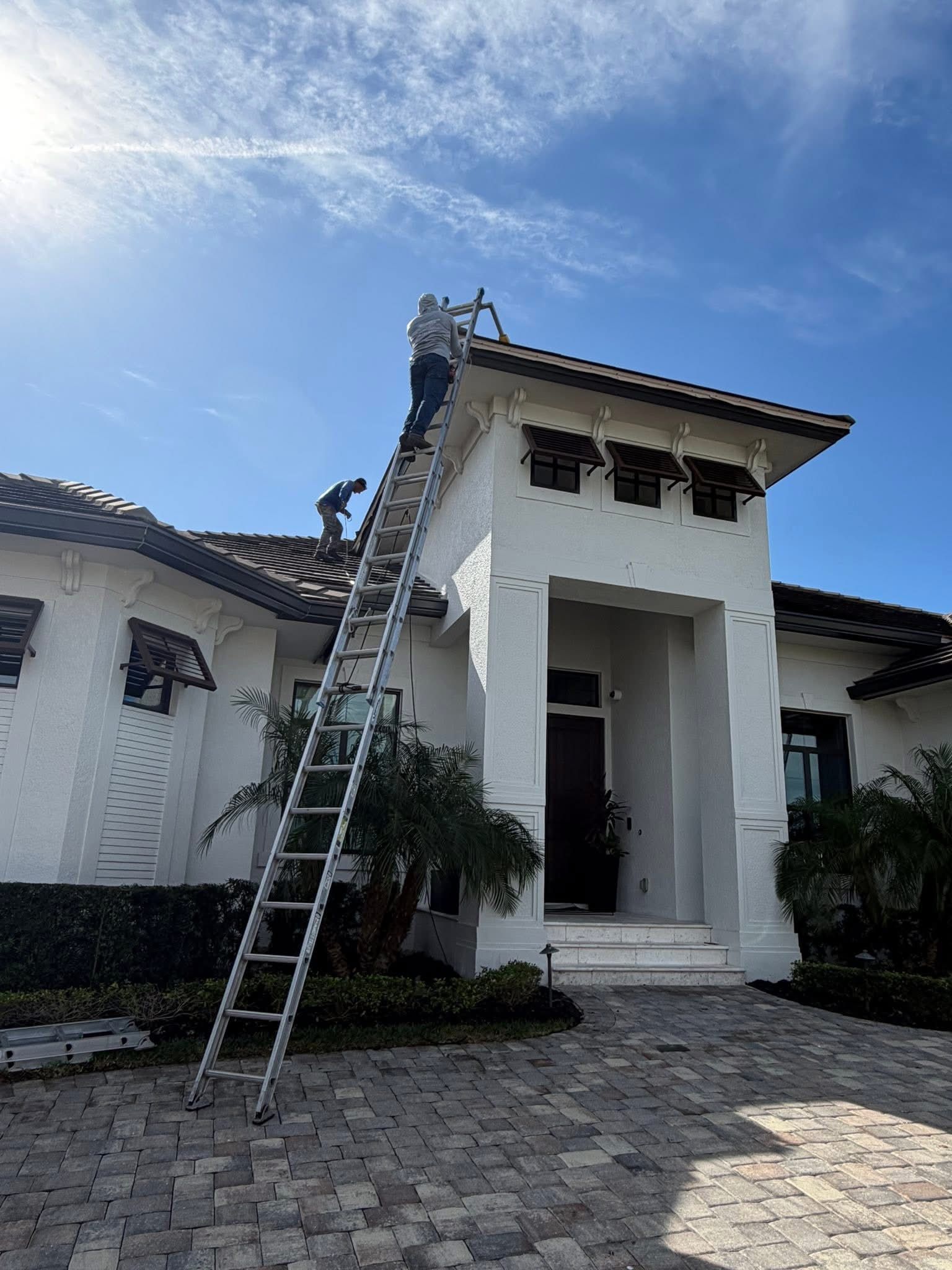 White Spanish-style house with a ladder leaning to the roof under a bright blue sky