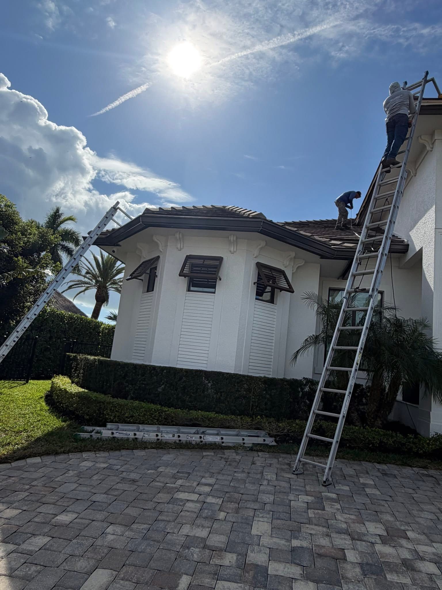 White house exterior with ladder beside roof under bright sunny sky