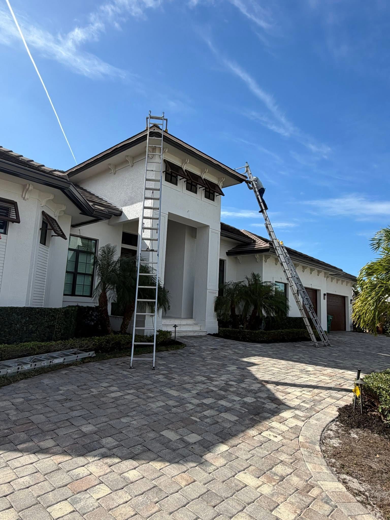 White stucco house with tiled roof, arched entry, and cobblestone driveway under a blue sky.