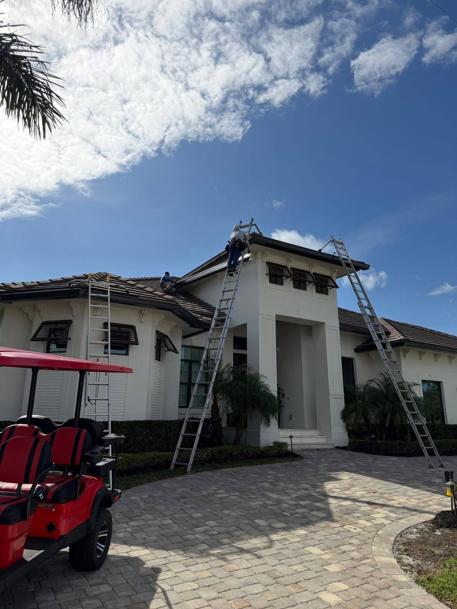 White stucco house with dark tile roof, cobblestone driveway, palm trees, and a red golf cart under a blue sky