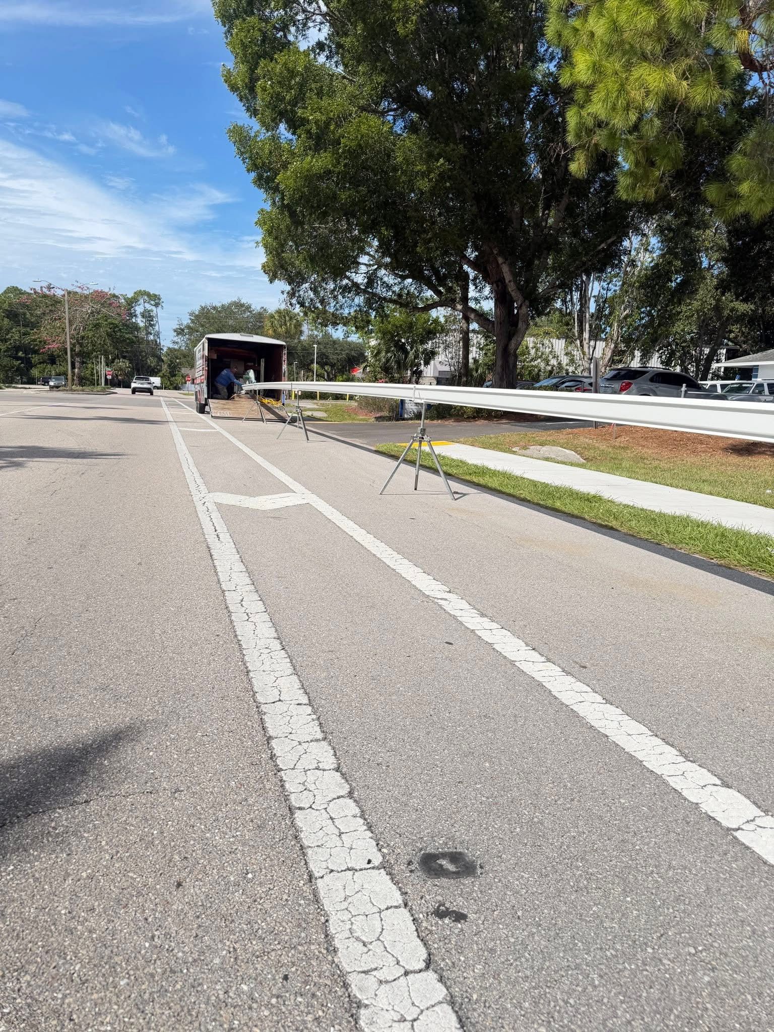 Empty road leading to a tunnel under a bright sky, with trees and parked cars on the right.