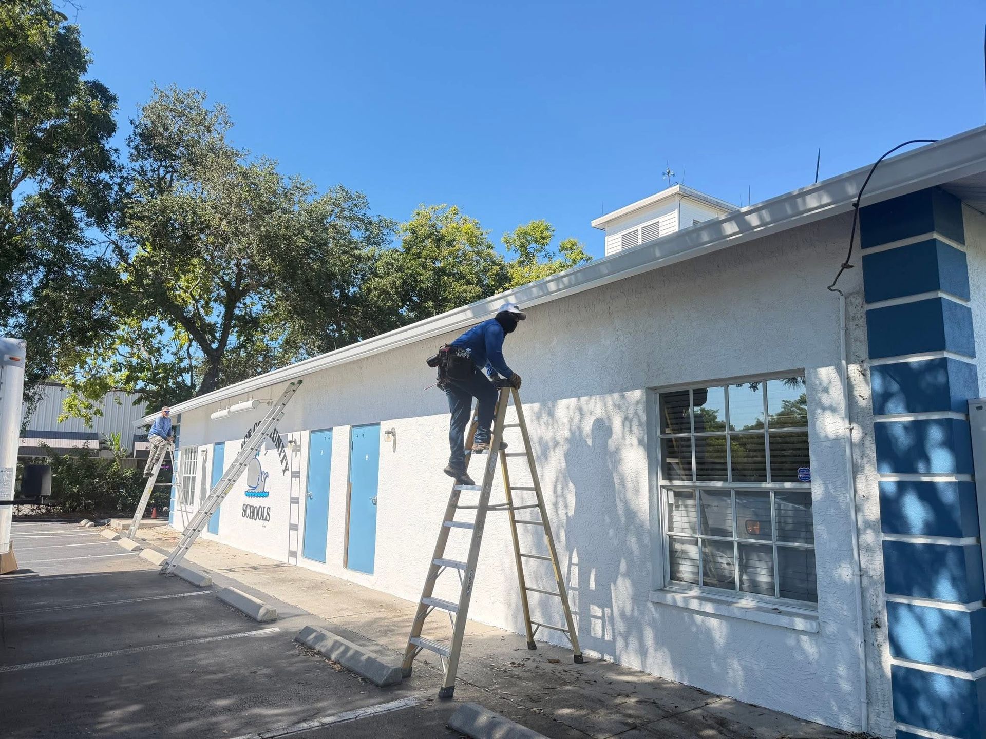 Worker on a ladder painting a white building exterior with blue trim