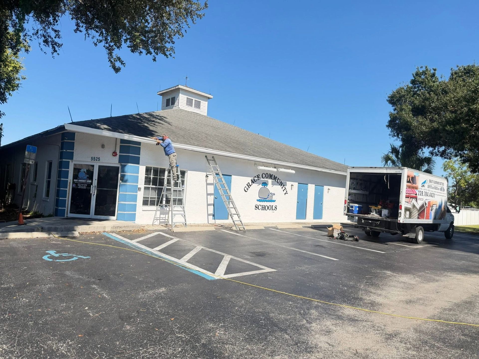 White building with blue stripes and a truck parked outside in a sunny parking lot
