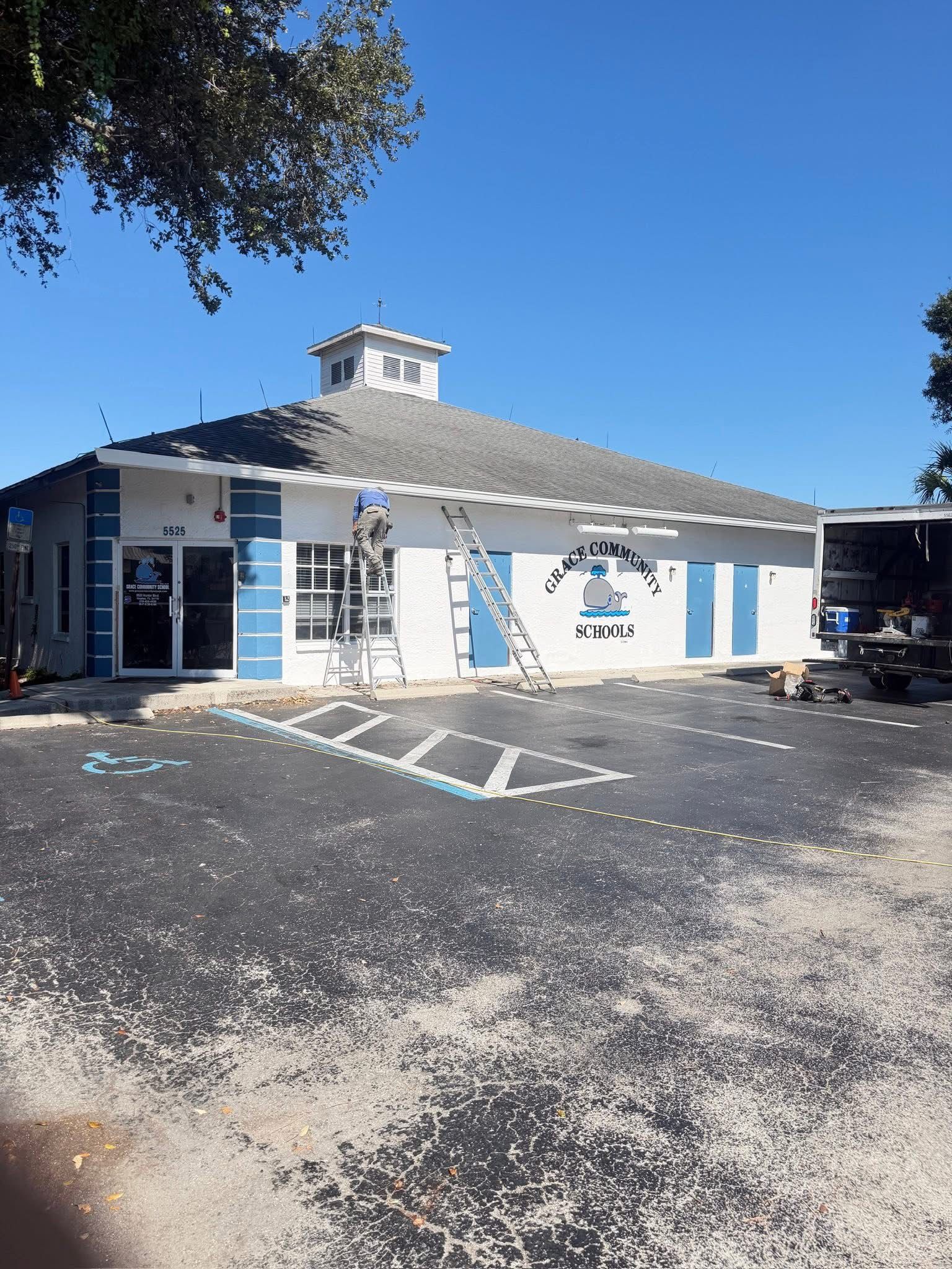 White building with blue shutters and a small tower, viewed from a parking lot under a clear blue sky.