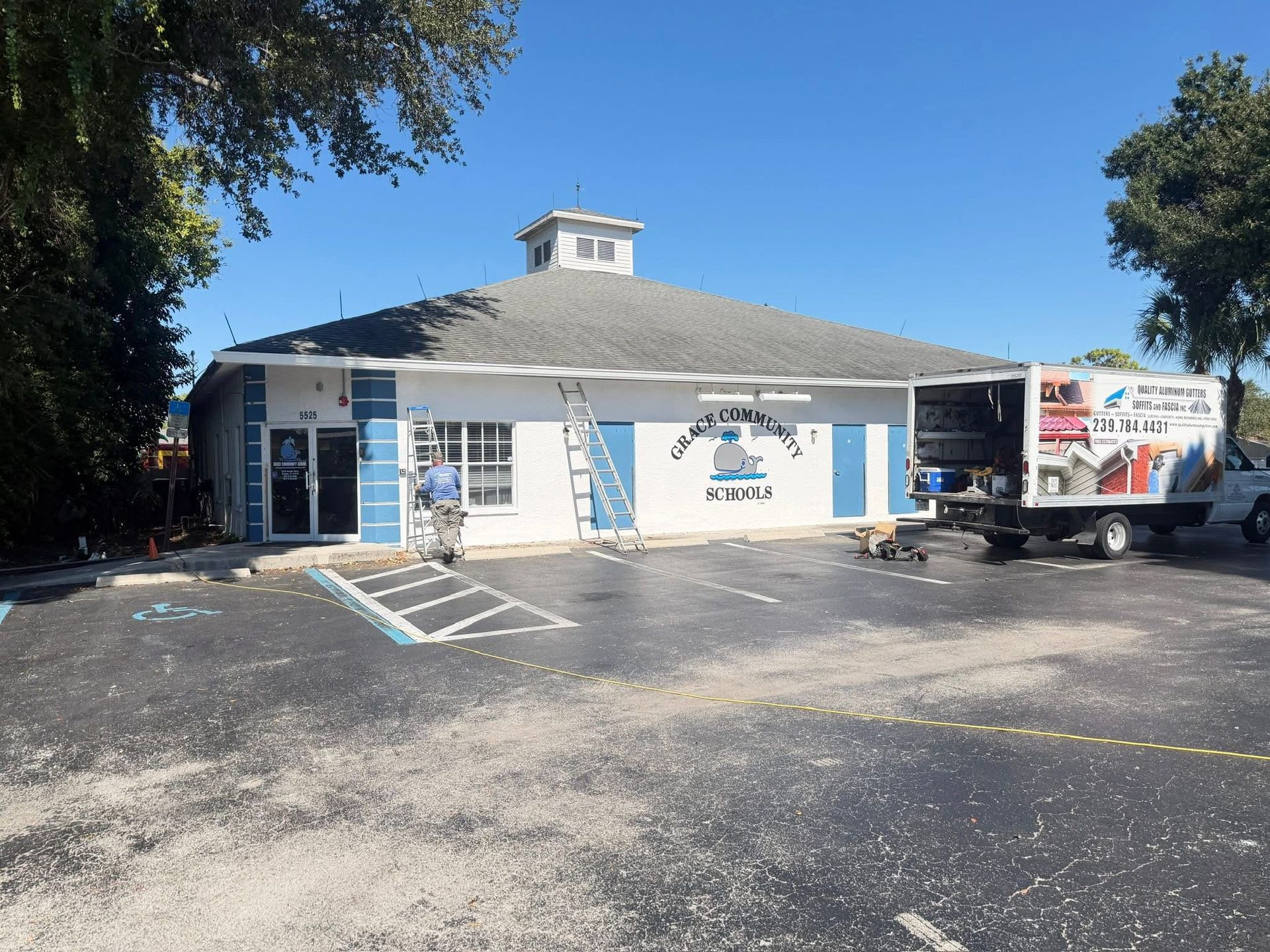 Small white storefront with a blue sign and a parked delivery truck on a sunny street