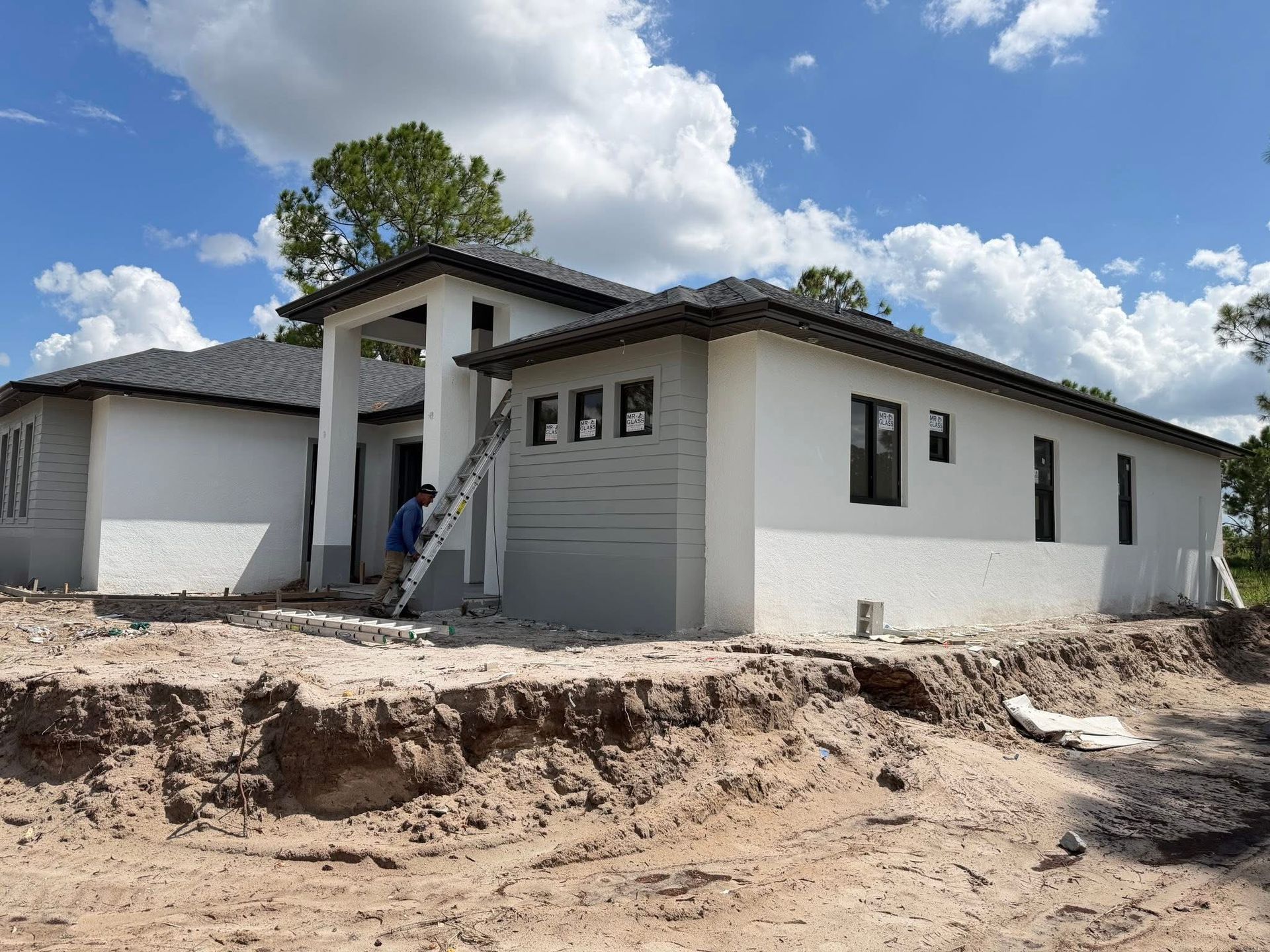 Modern white house under construction with a garage and sandy foreground under a blue sky