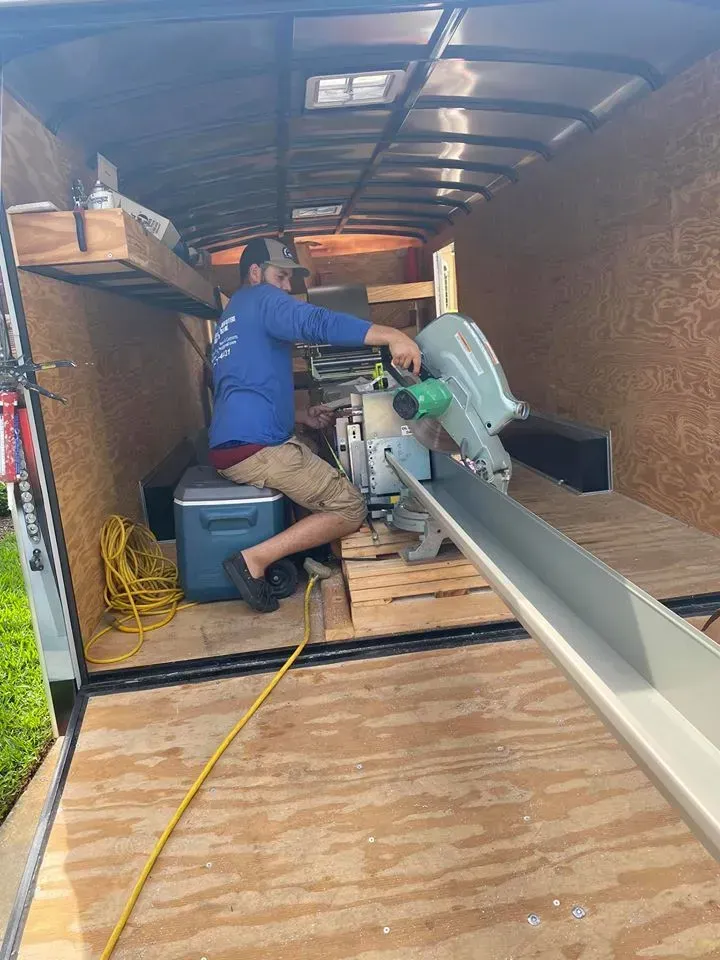 Person using a miter saw inside a trailer workshop, cutting a long board.
