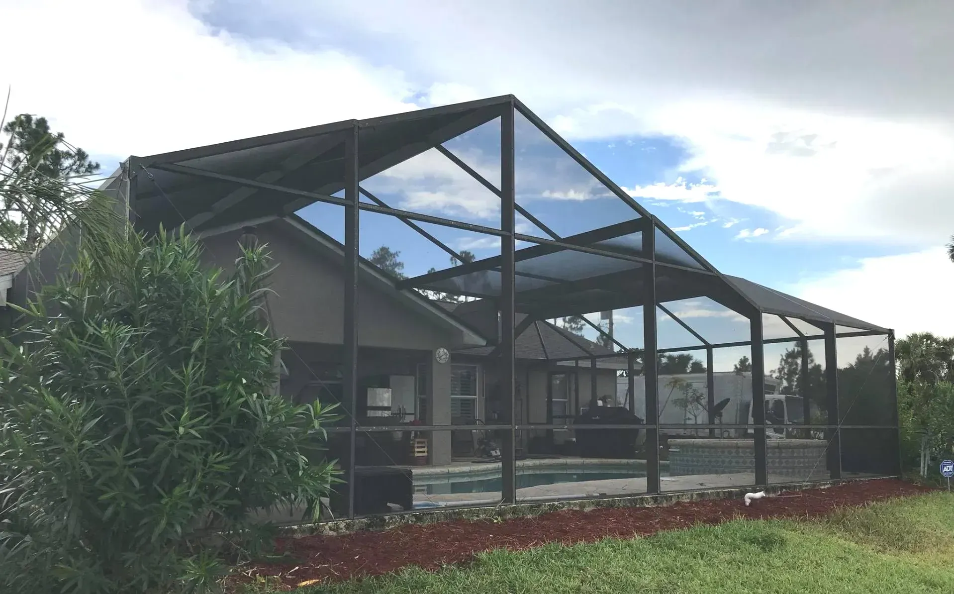 Covered outdoor patio with metal pergola beside a house and garden greenery