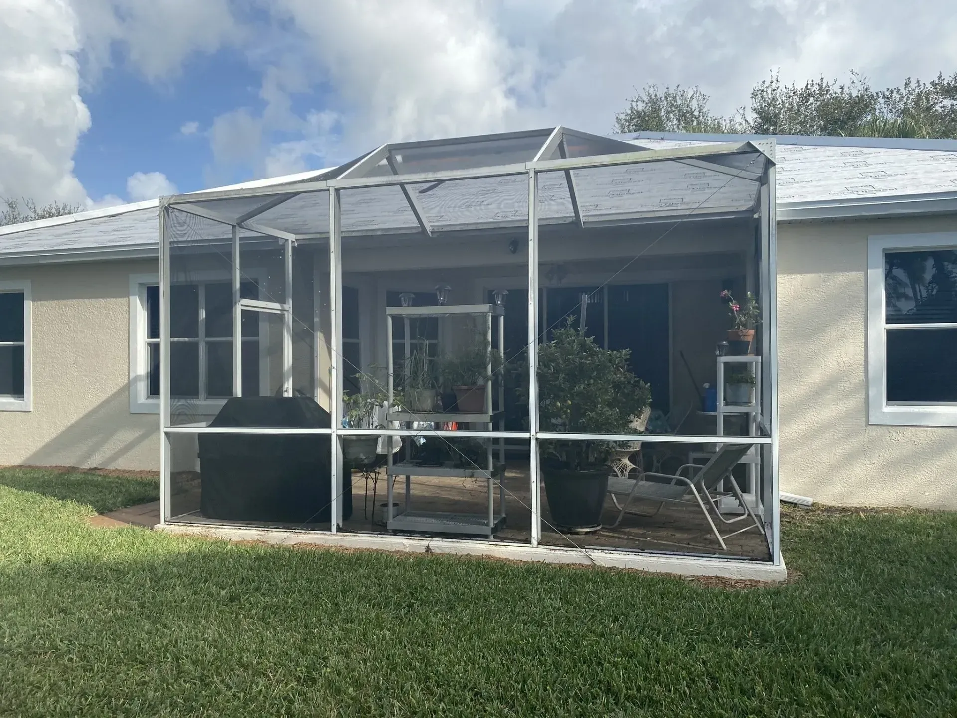 Screened patio attached to a house with outdoor table and chairs on a grassy lawn.