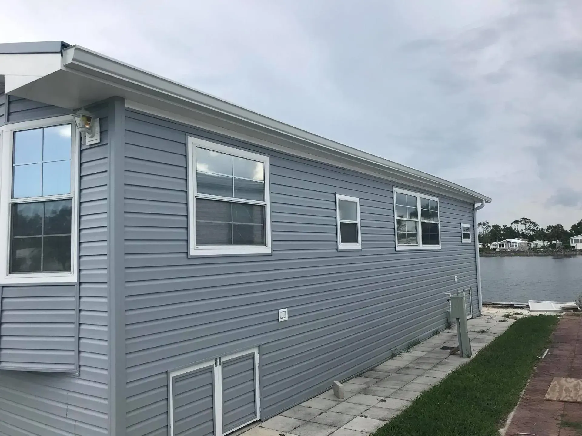 Gray house exterior with windows and side walkway beside a grassy yard by the water