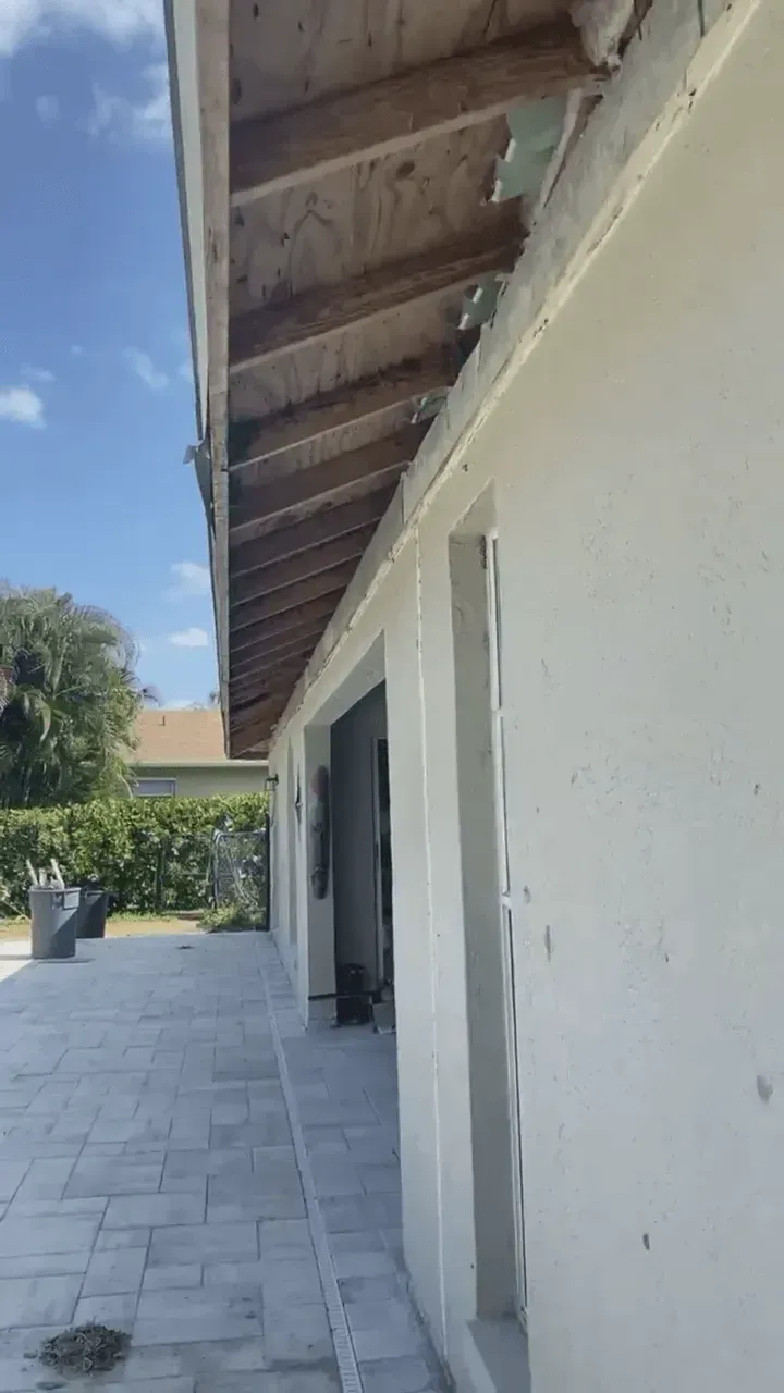 Outdoor patio beside a white stucco building with a wooden roof overhang and open doorway.