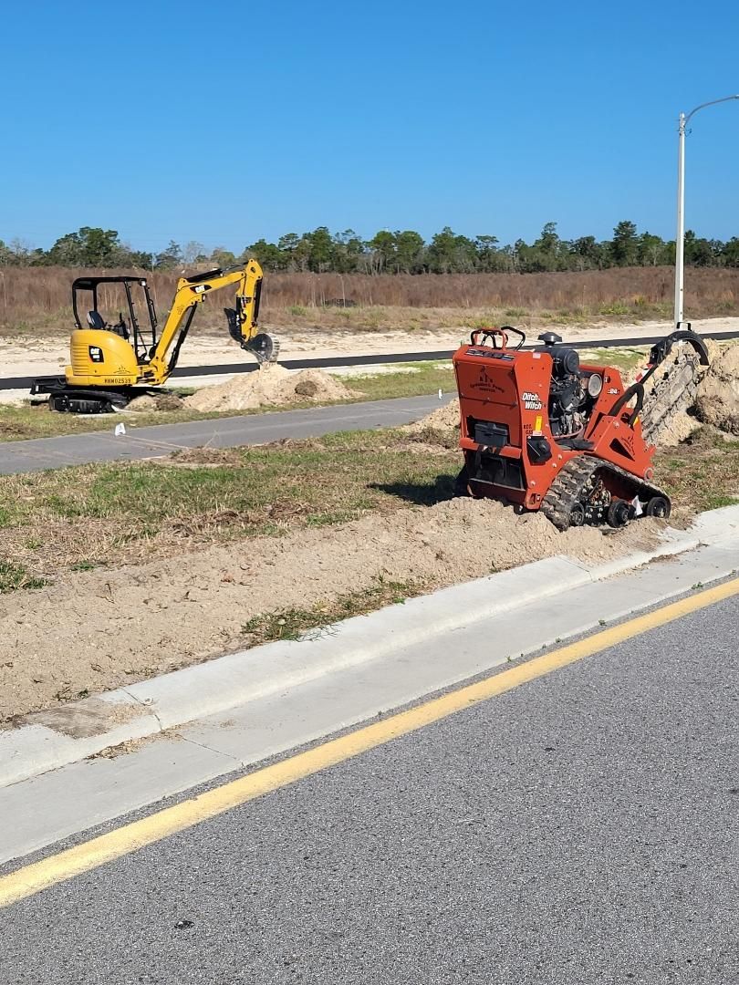 A small yellow excavator is sitting on the side of the road next to a small orange machine.