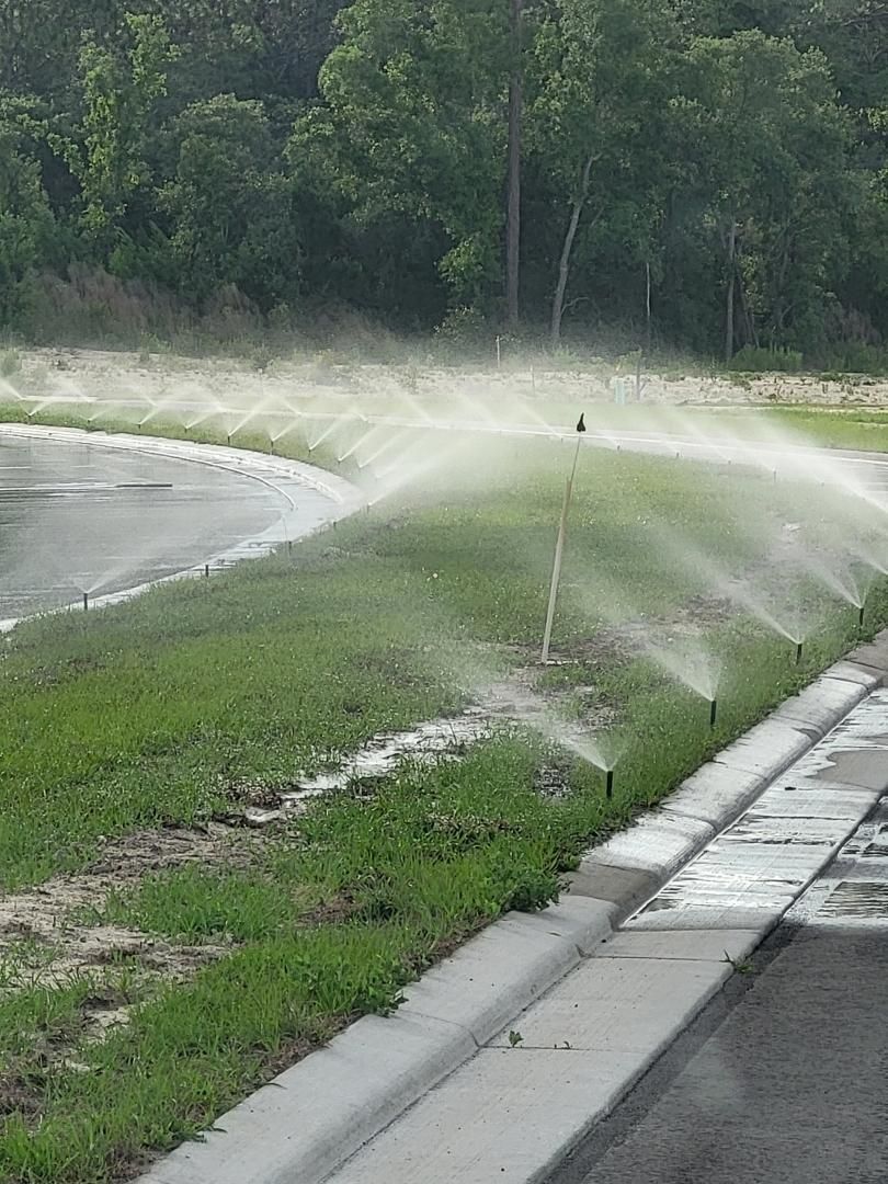 A row of sprinklers spraying water on a lush green lawn.