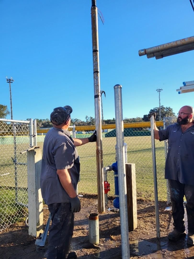 Two men are working on a pole in a field