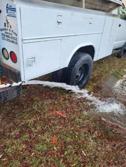 A white truck is parked in the grass with water coming out of it.