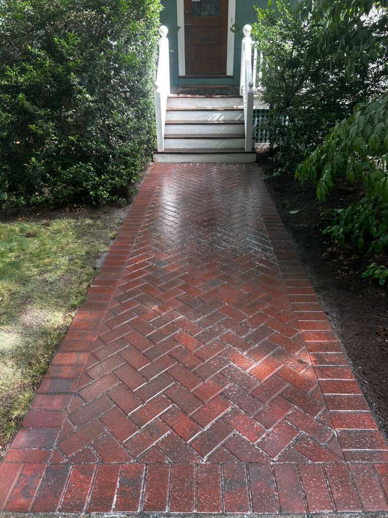 Red brick walkway leading to a front stoop, bordered by green hedges.